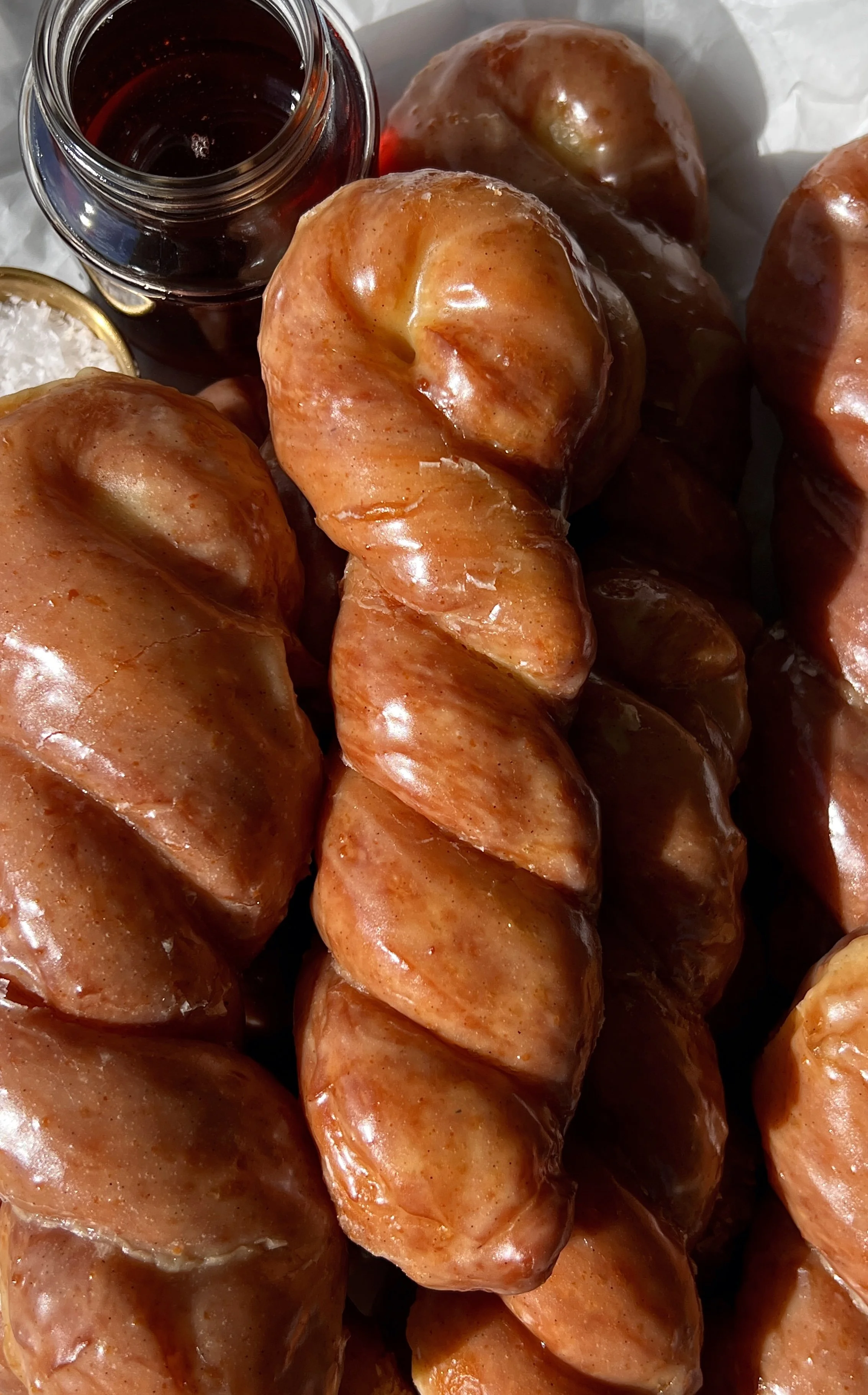 Close-up of a brown butter maple twist donut showing the perfectly golden exterior with a slight chew and pillowy soft milk bread interior glazed in a rich brown butter maple glaze.