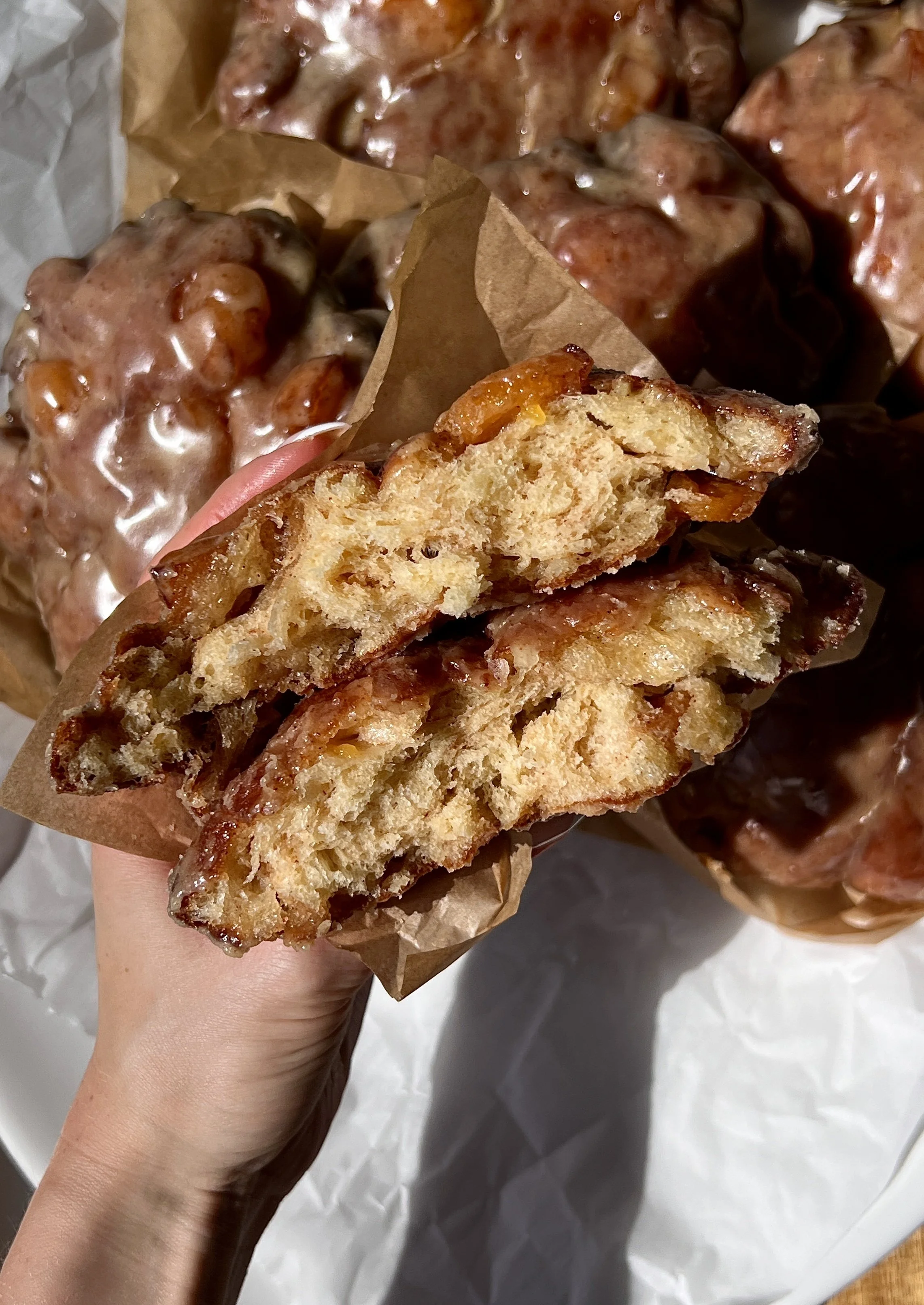 Close-up of a golden and crisp peach fritter donut with a soft and fluffy interior and warm gooey peach filling laced throughout coated in a silky brown butter maple vanilla bean glaze.