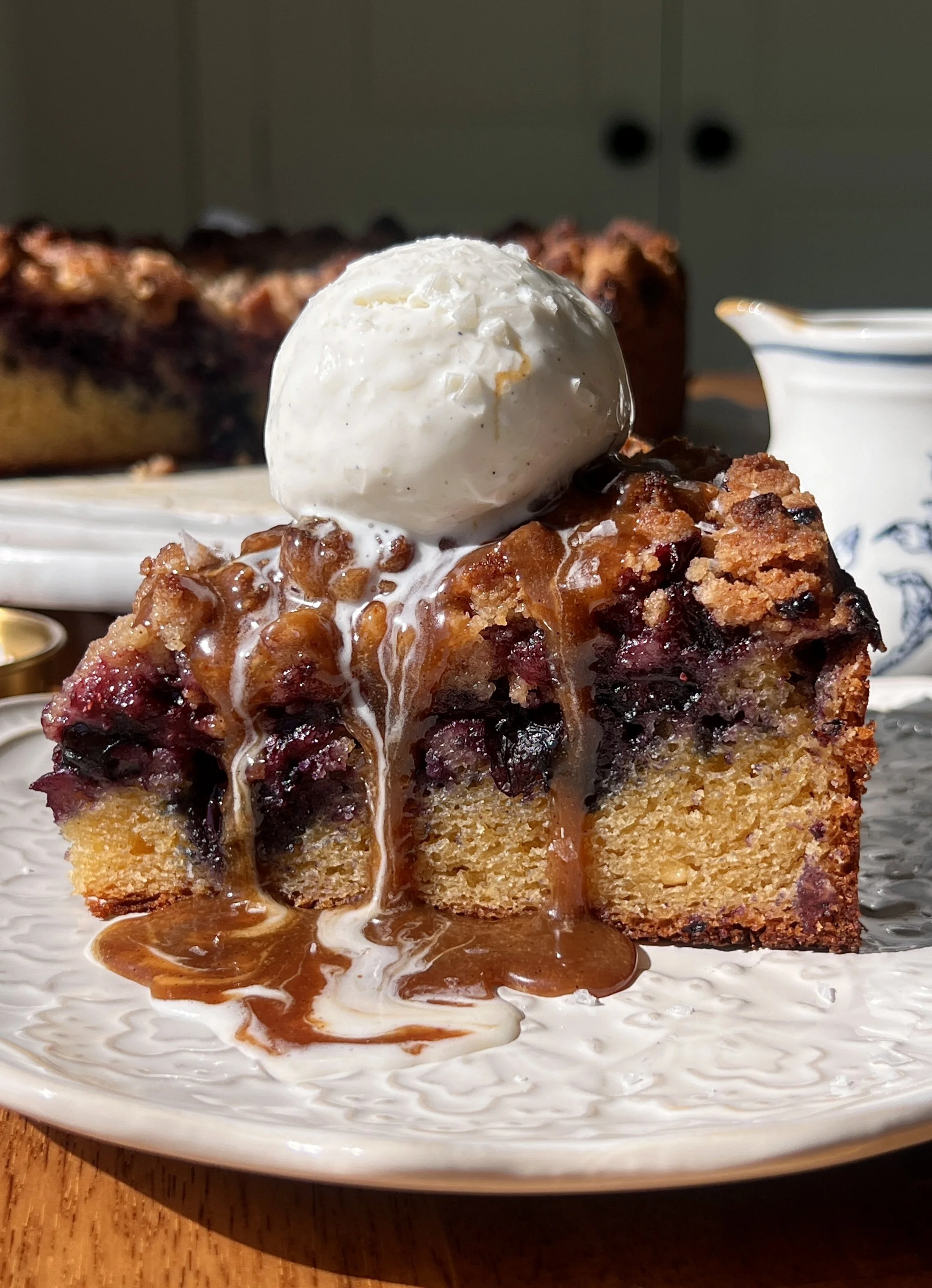 Brown butter blueberry crumble cake with a golden buttery crumble topping served warm with a scoop of vanilla ice cream and a hot cup of coffee.