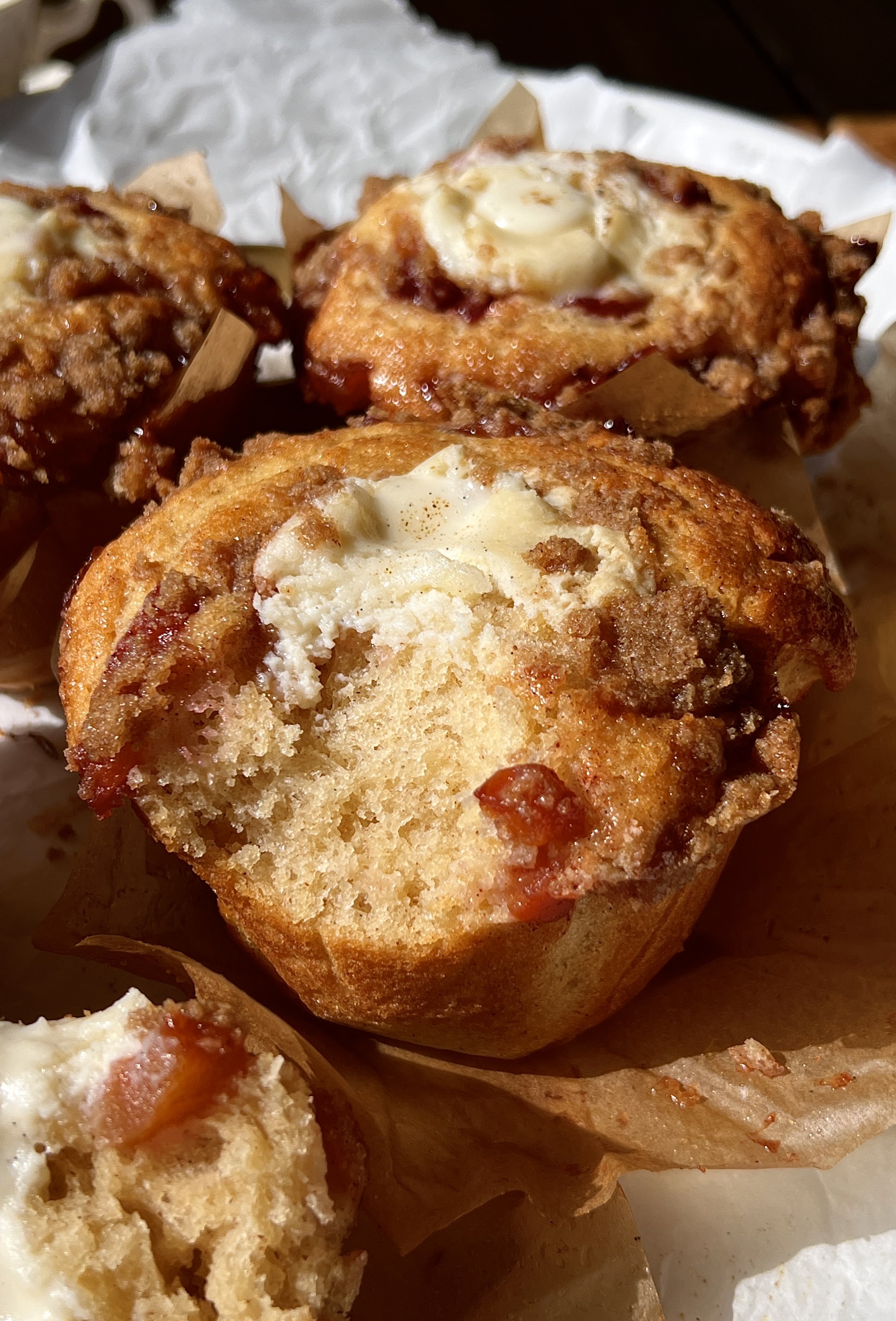 Bakery-style peach cobbler cream cheese muffin with a bite taken out showing the soft fluffy crumb, bright peach flavor, and rich tangy cream cheese center inside.