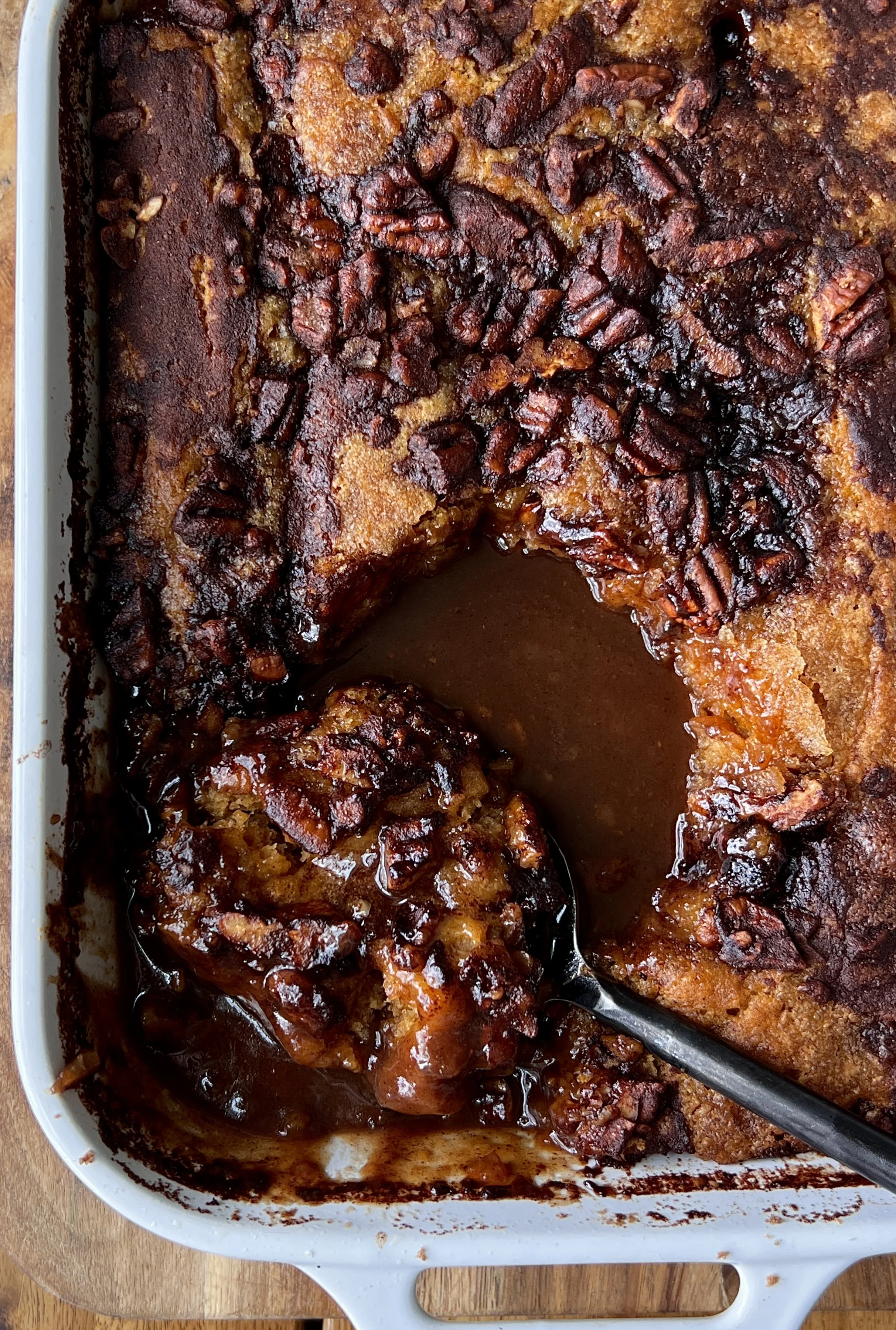 Golden brown butter sweet potato pecan cobbler with a gooey base and crisp top, topped with vanilla ice cream and a sprinkle of flaky sea salt, served warm in a baking dish with pecans scattered around.