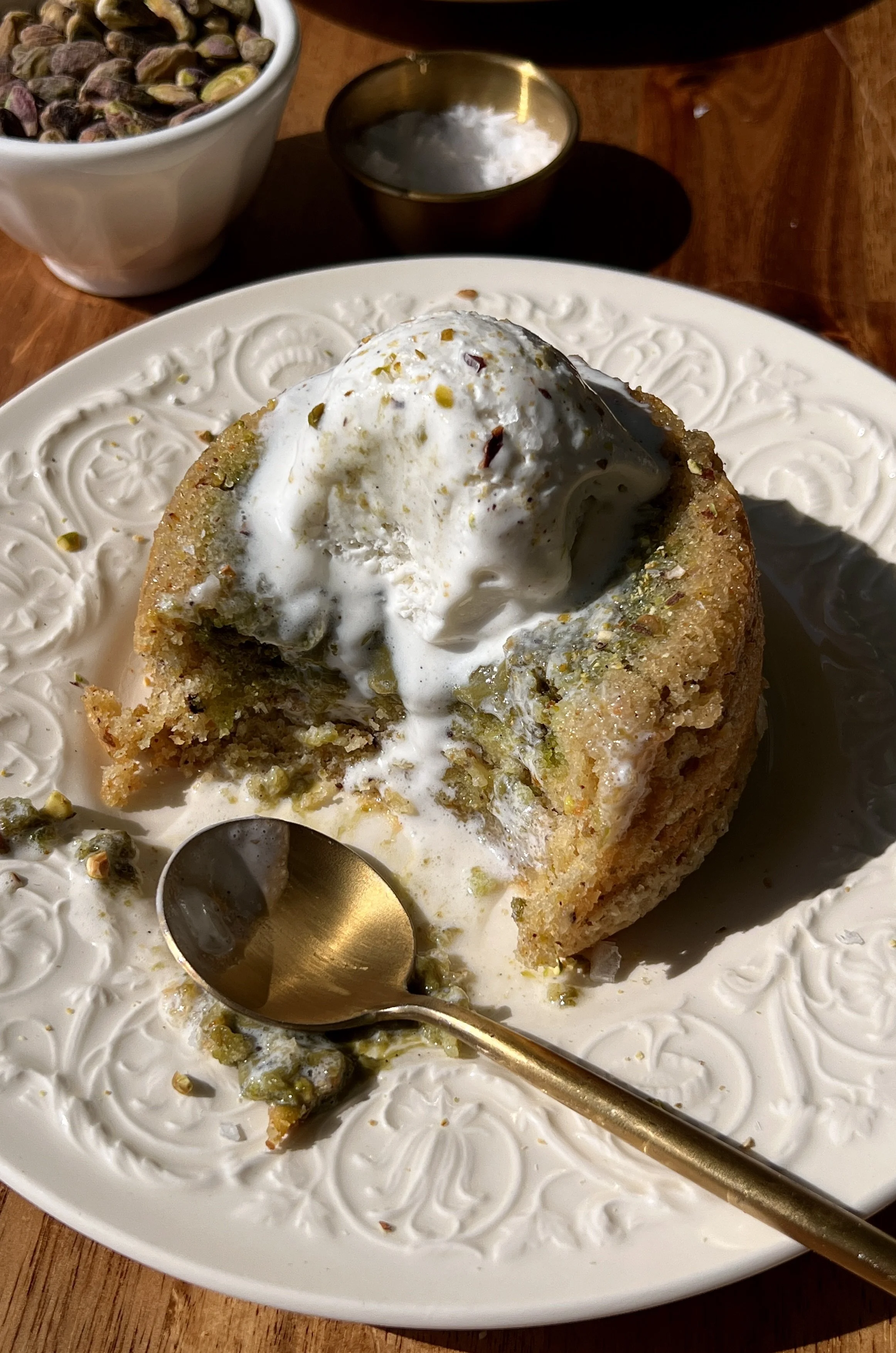 Pistachio cream lava cake cut open showing the warm and gooey molten pistachio cream center flowing out served with a scoop of vanilla ice cream.