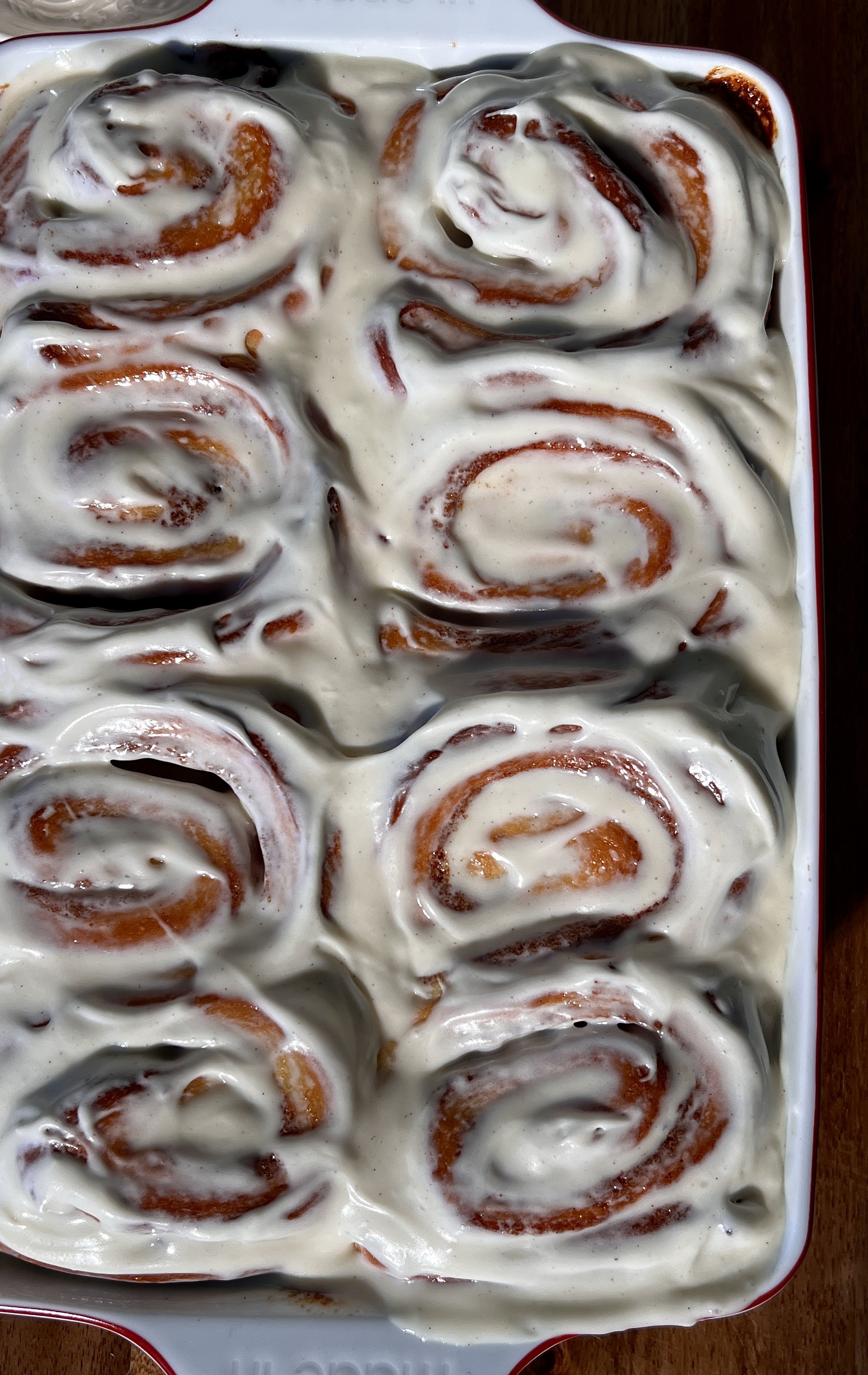 Soft, gooey eggnog cinnamon rolls in a baking dish, swirled with a golden brown sugar cinnamon filling and topped with melting eggnog cream cheese frosting.