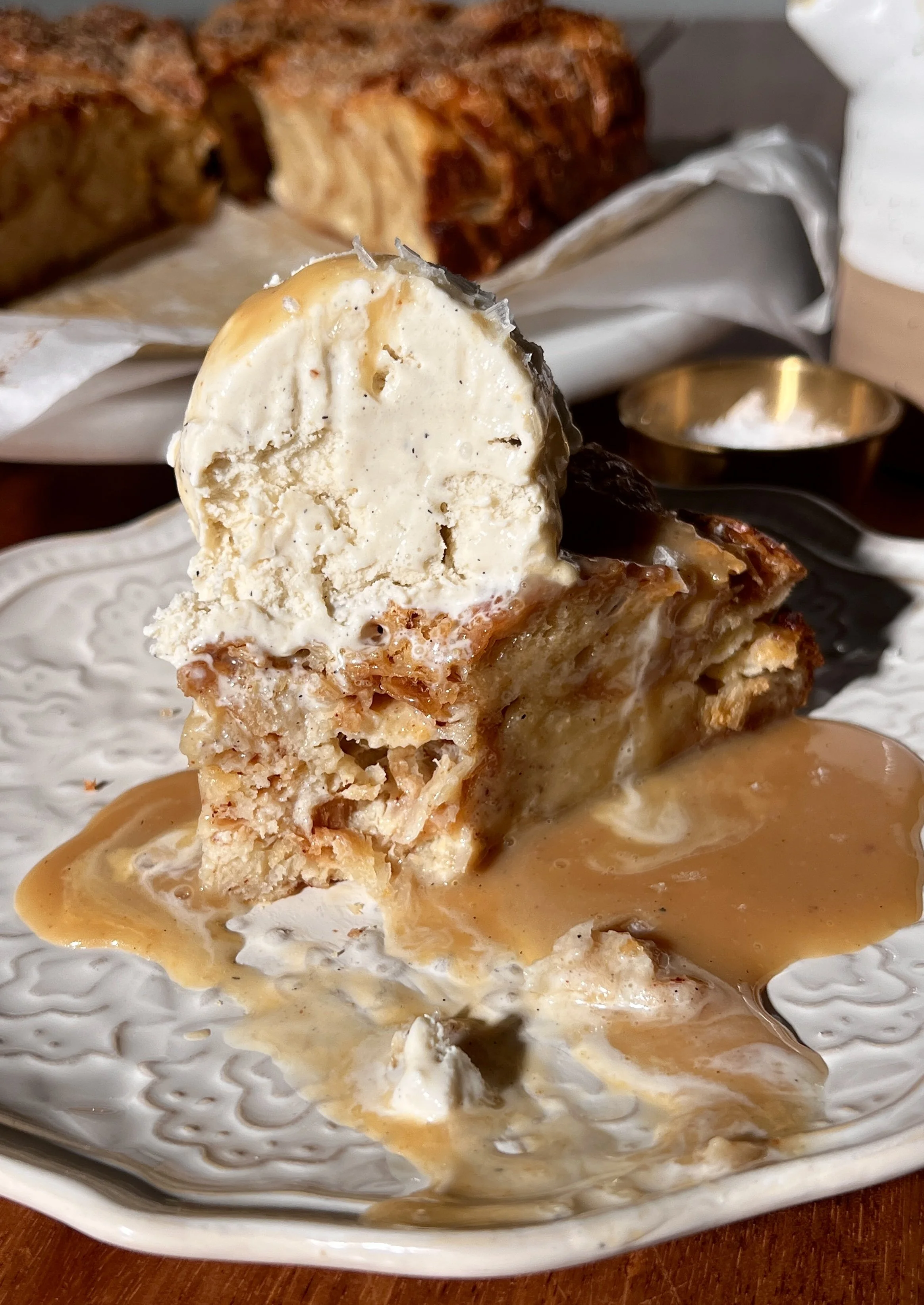 Warm vanilla bean croissant bread pudding with a golden crisp top, served with buttered caramel rum sauce and a scoop of vanilla ice cream.