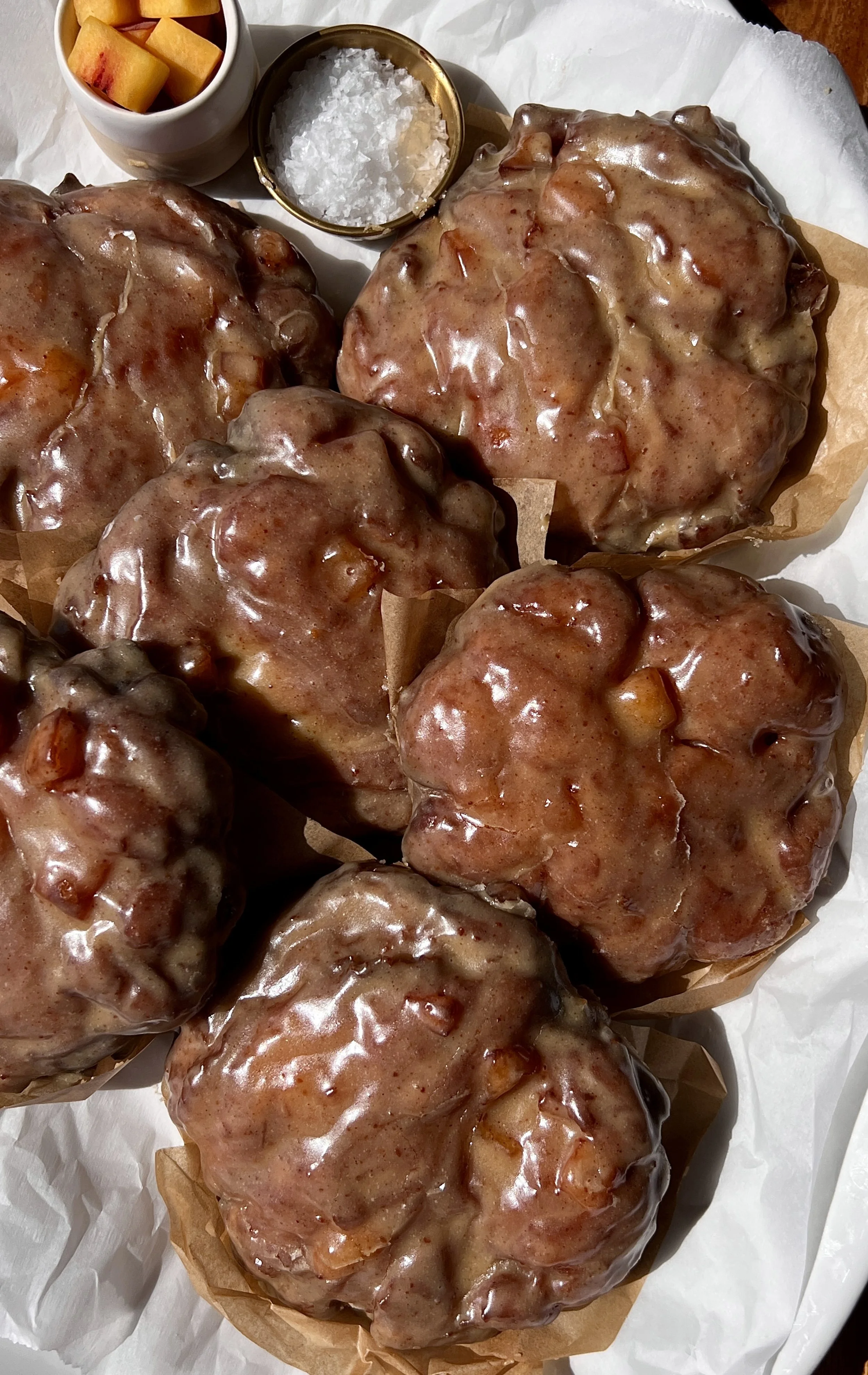 Peach fritter donuts coated in a silky brown butter maple vanilla bean glaze served warm with a hot cup of coffee.