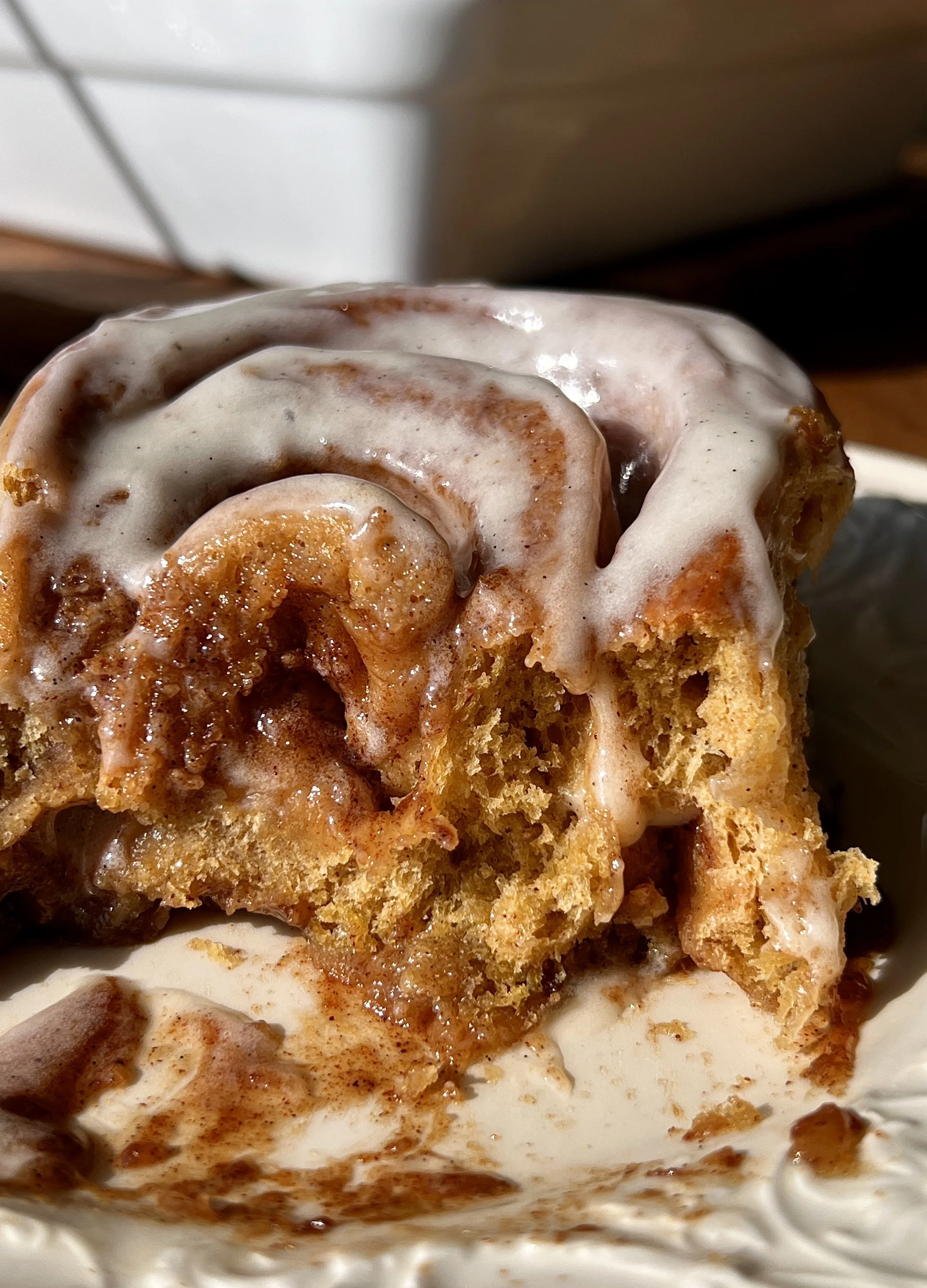 Close-up of a soft and fluffy homemade pumpkin cinnamon roll with beautifully golden caramelized edges and a warming gooey pumpkin spice cinnamon filling with cream cheese frosting melting into every swirl.