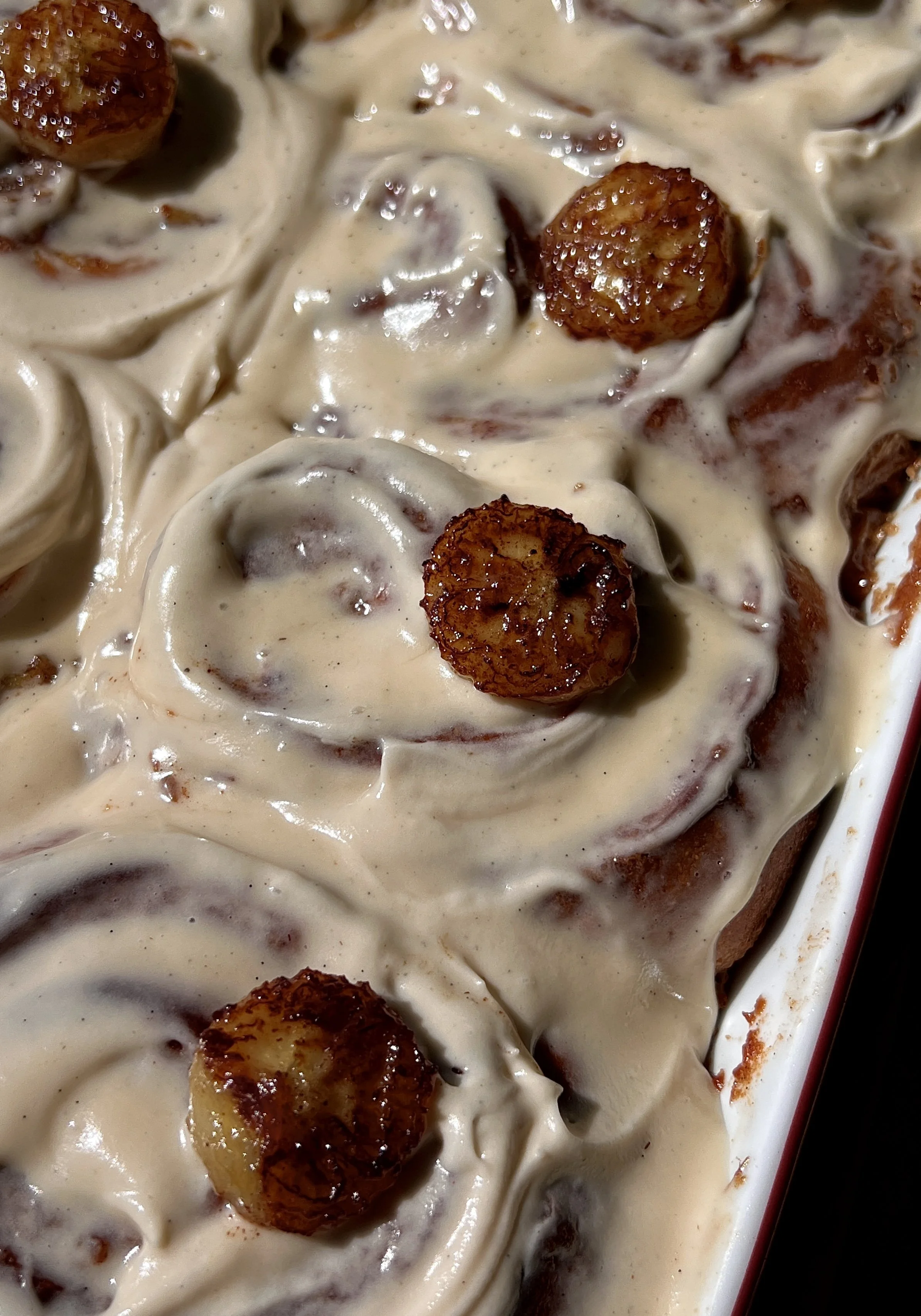 Close-up of a soft and fluffy banana bread buttermilk cinnamon roll with a gooey banana bread cinnamon filling and honey brown sugar cream cheese frosting melting into every swirl.