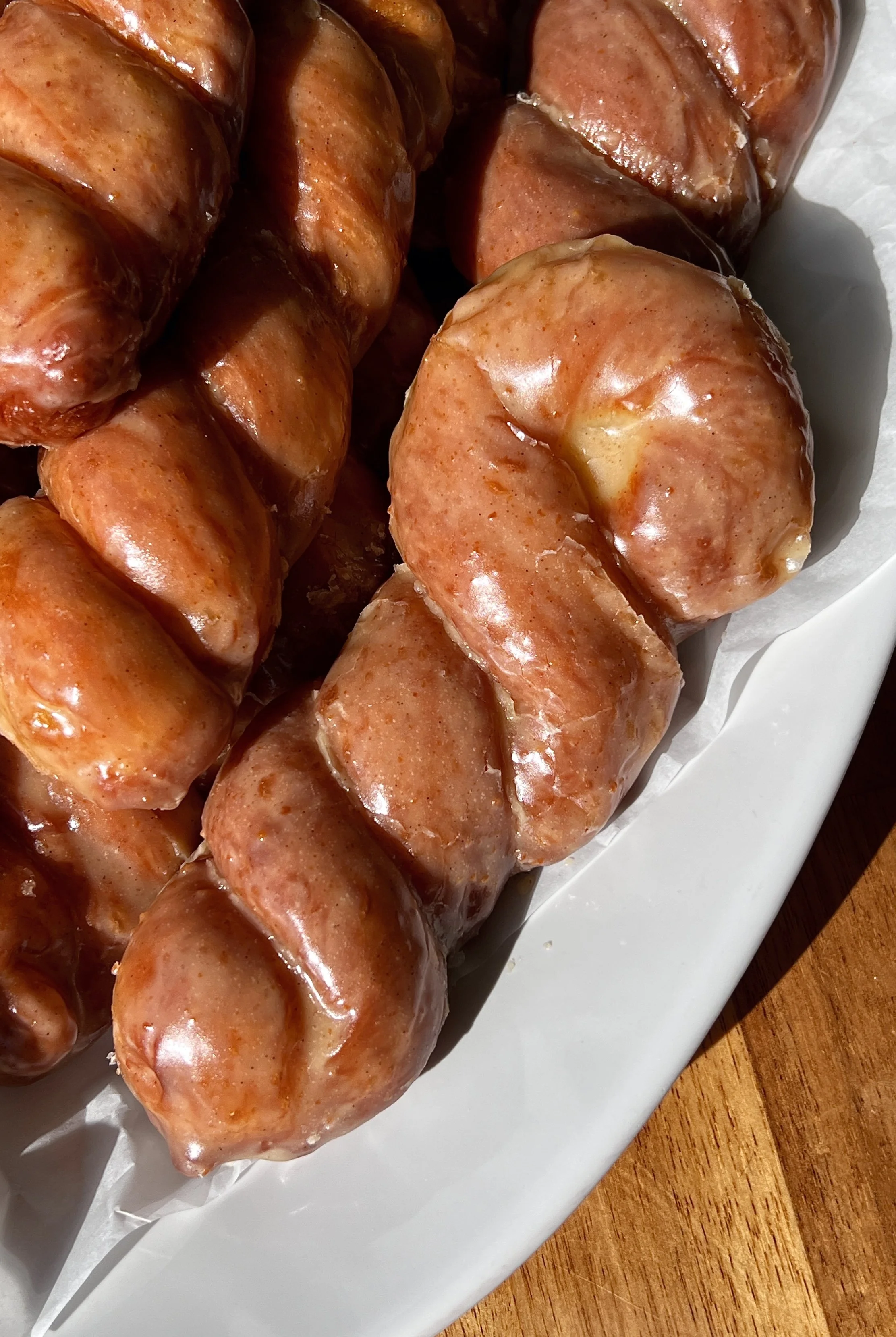 Close-up of a brown butter maple twist donut showing the perfectly golden exterior with a slight chew and pillowy soft milk bread interior glazed in a rich brown butter maple glaze.