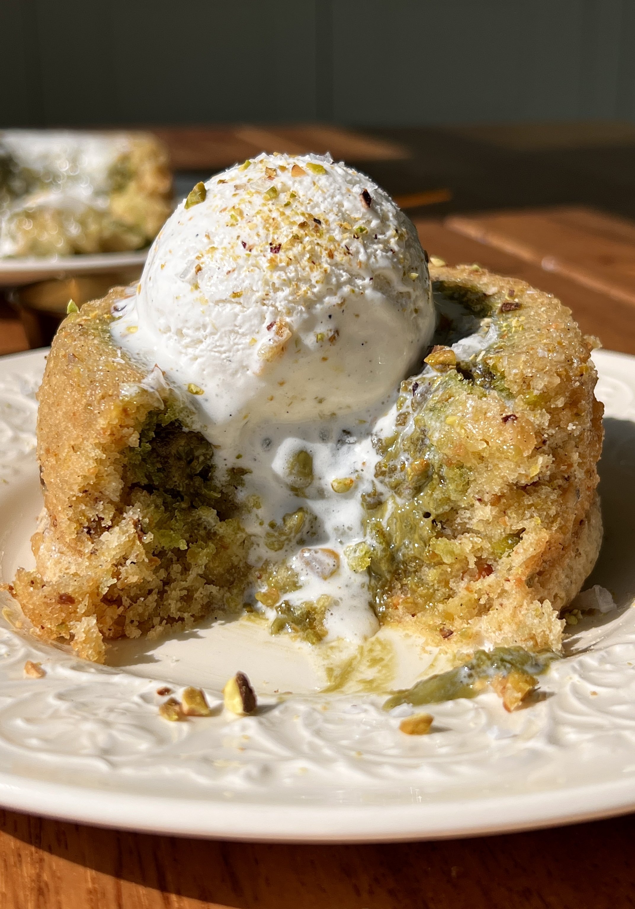 Pistachio cream lava cake cut open showing the warm and gooey molten pistachio cream center flowing out served with a scoop of vanilla ice cream.