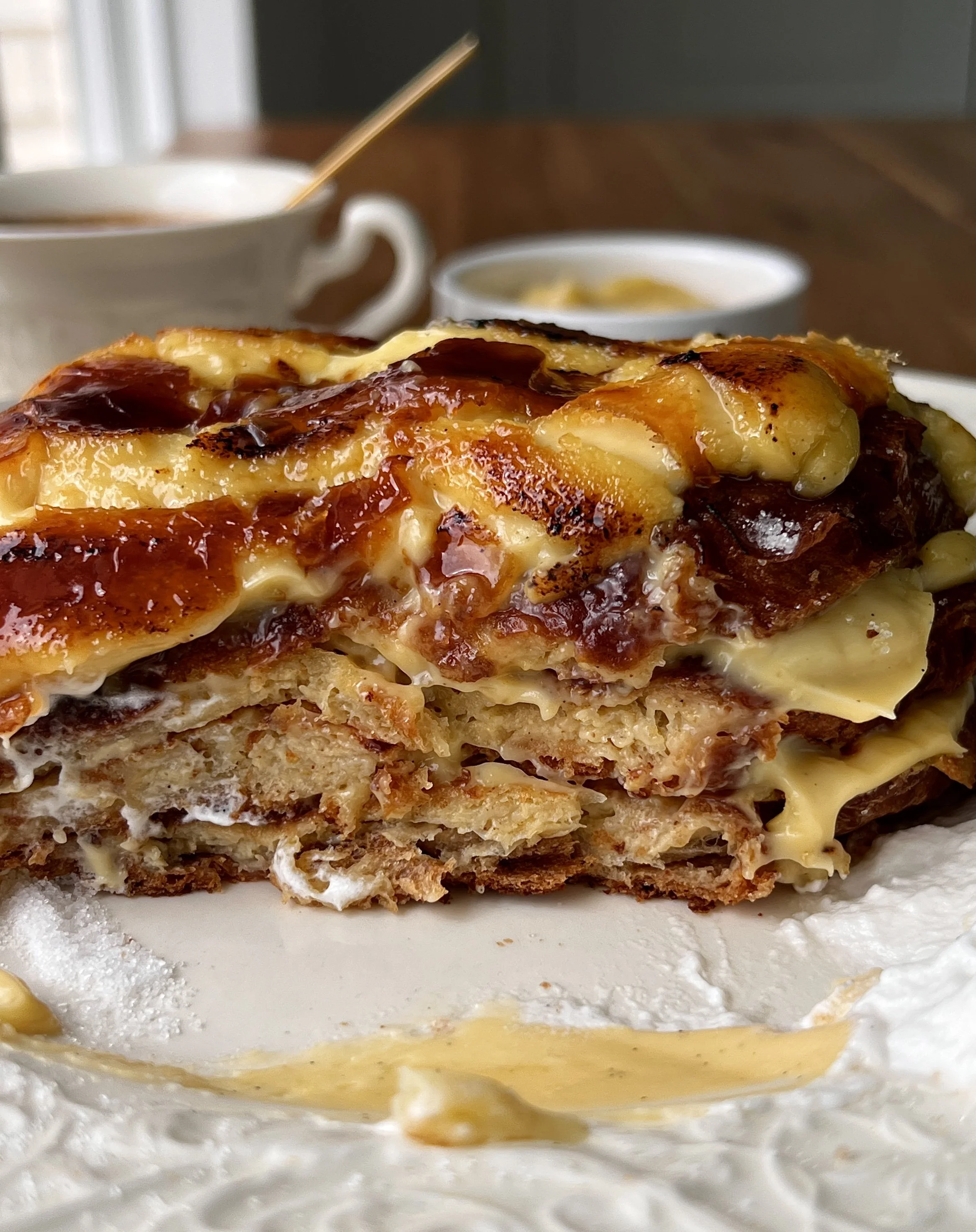 Crème brûlée croissant french toast with a crisp caramelized sugar layer being cracked open revealing the rich and creamy vanilla bean custard and golden buttery croissant underneath.