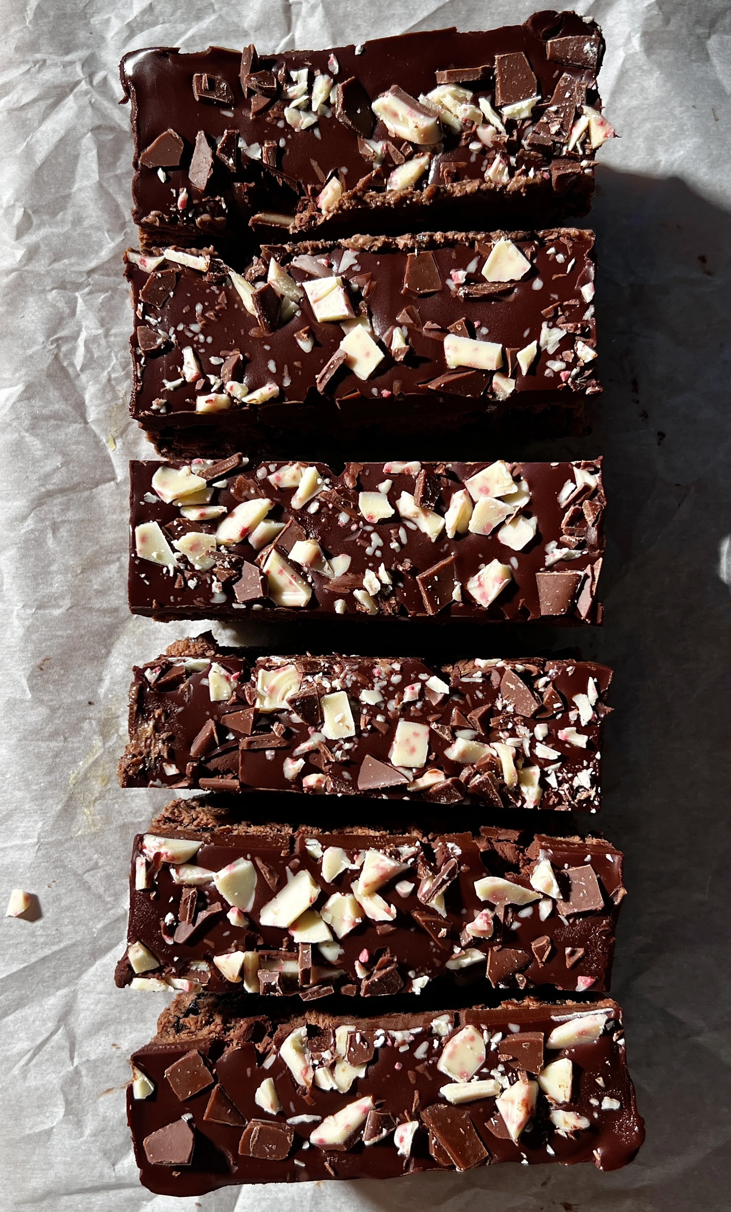 Close-up of peppermint Oreo cheesecake bars with a dark Oreo crust, creamy peppermint mocha cheesecake filling, chocolate ganache topping, and chopped peppermint bark sprinkled on top.