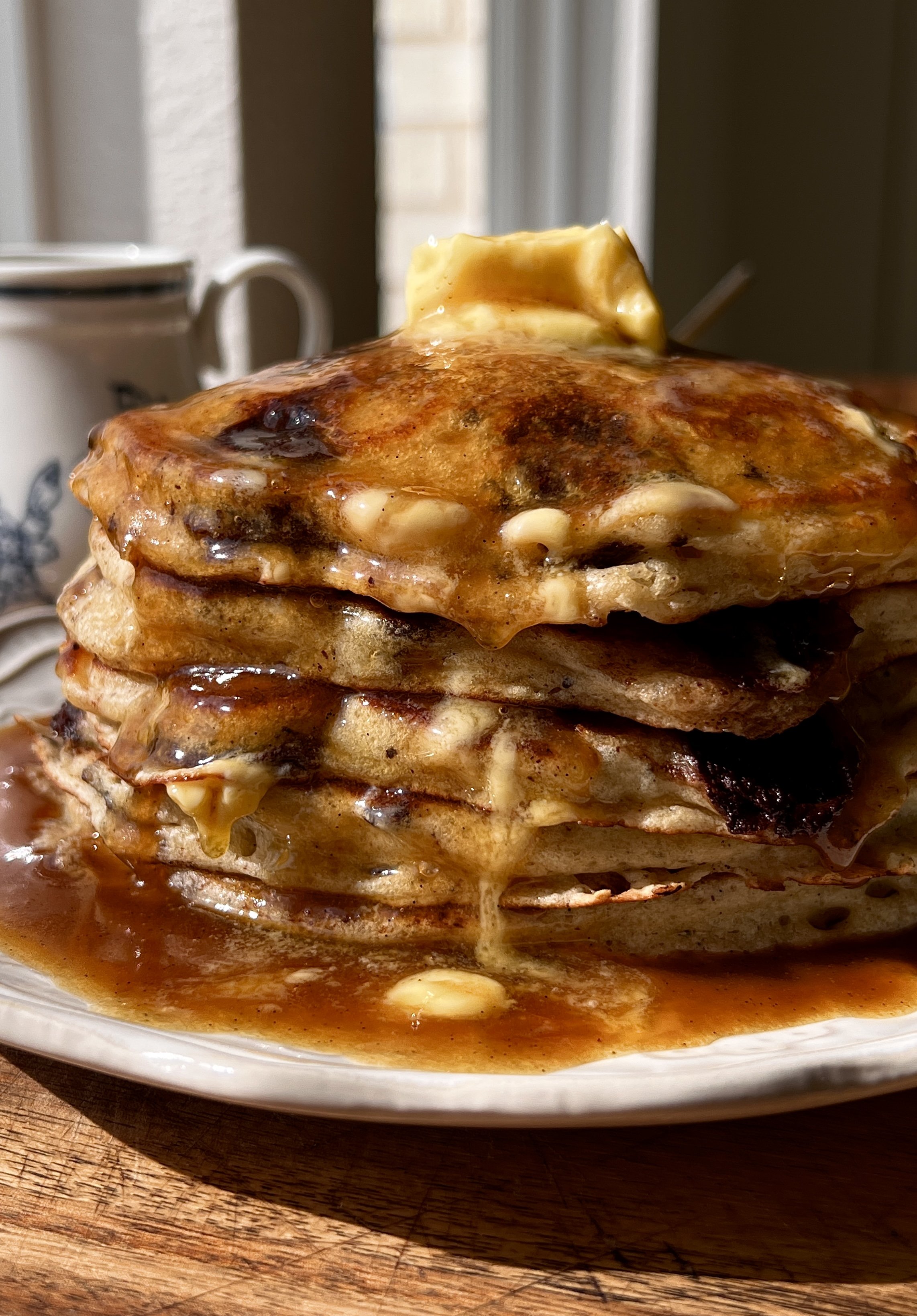Brown butter chocolate chip pancakes stacked and drizzled with maple espresso buttermilk syrup and a pat of butter.