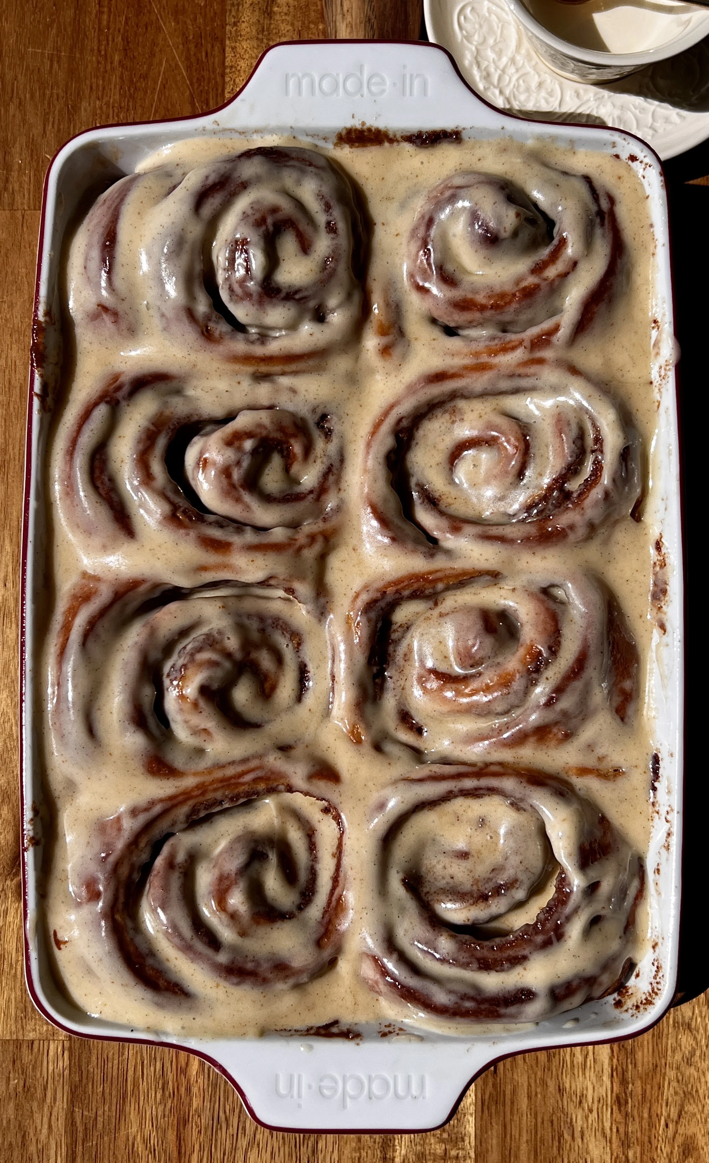 Pan of golden brown butter buttermilk cinnamon rolls with sticky caramelized edges topped with smooth brown butter cream cheese frosting melting into every swirl.