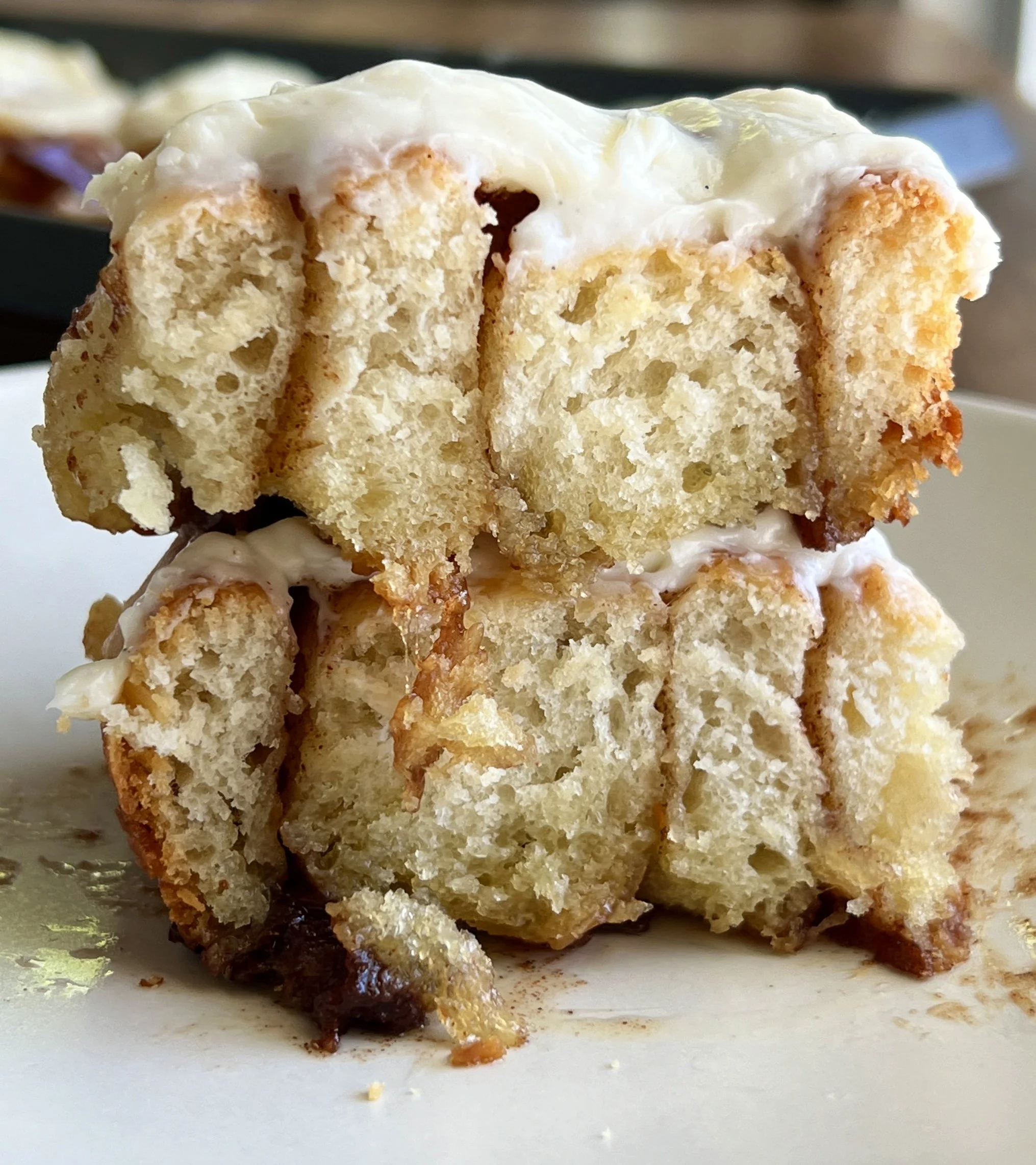Close-up of Sourdough Cinnamon Rolls with a golden exterior, topped with cream cheese icing. The fluffy rolls are swirled with cinnamon sugar filling, promising a decadent treat. The icing adds a creamy finishing touch to these homemade delights.