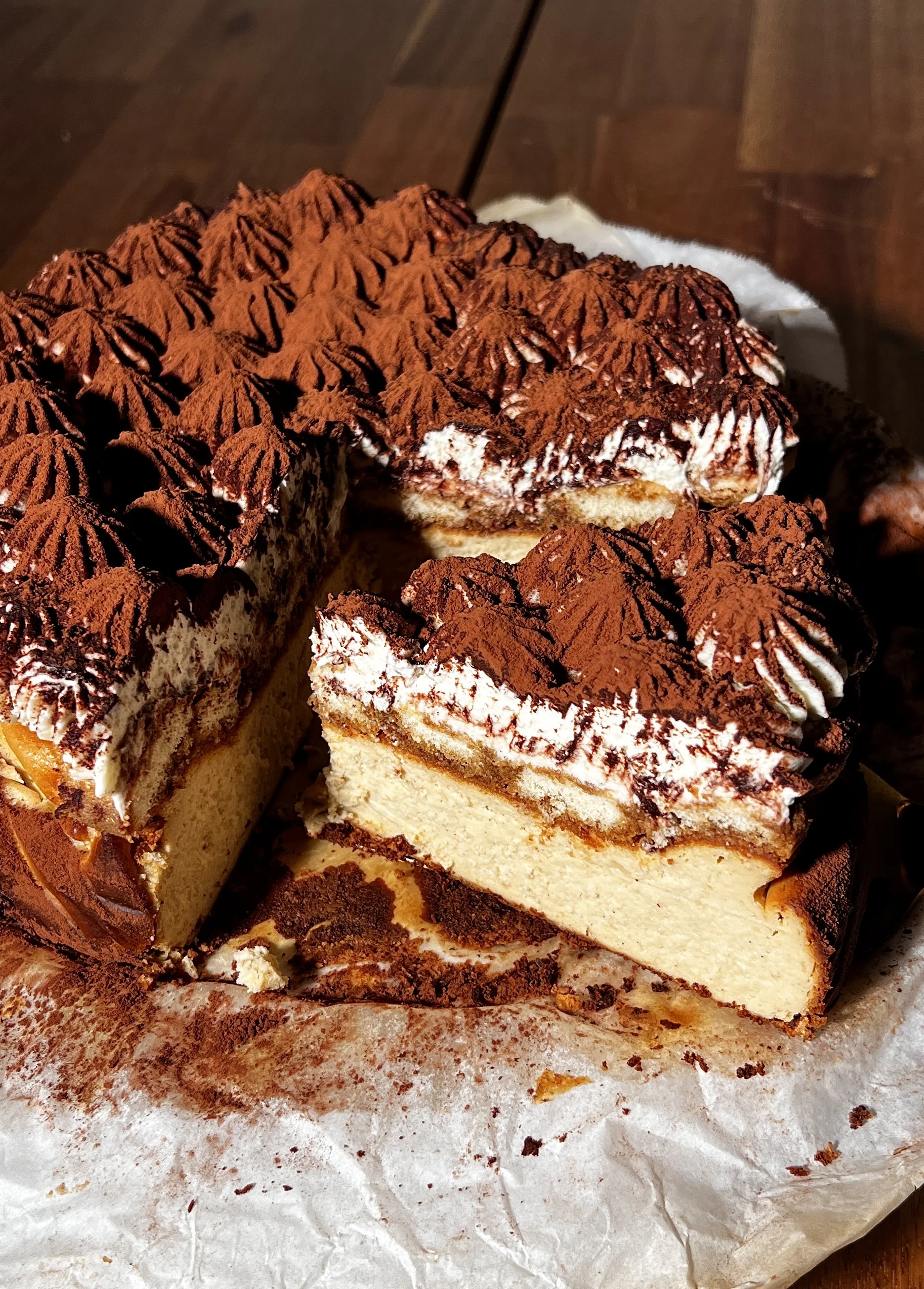 Tiramisu basque cheesecake topped with espresso-soaked ladyfingers, creamy mascarpone layer, and a generous dusting of cocoa powder.