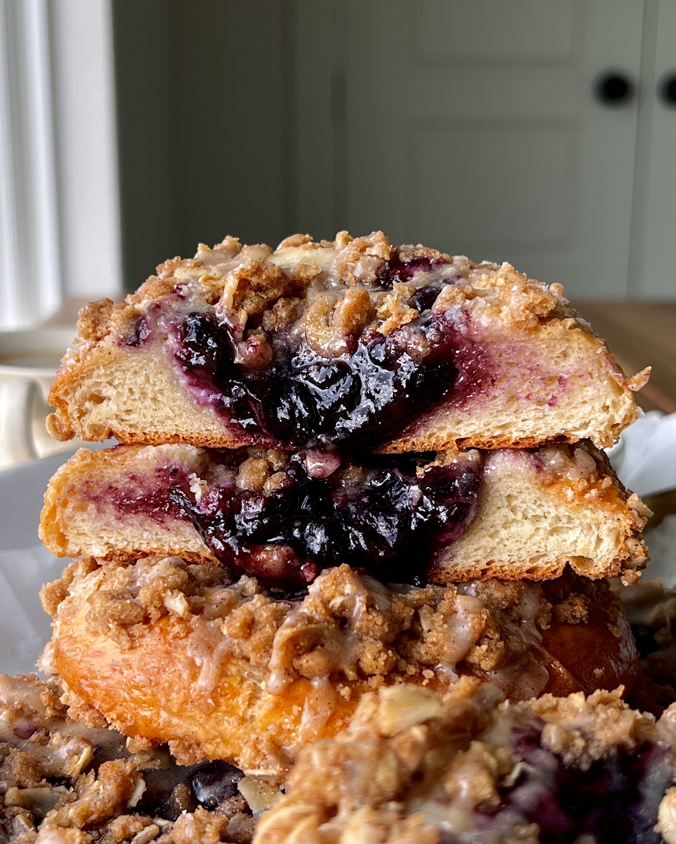 Close-up of a soft and pillowy blueberry cheesecake streusel bun with a rich and tangy cheesecake filling, homemade jammy blueberry compote, and golden oat streusel throughout.