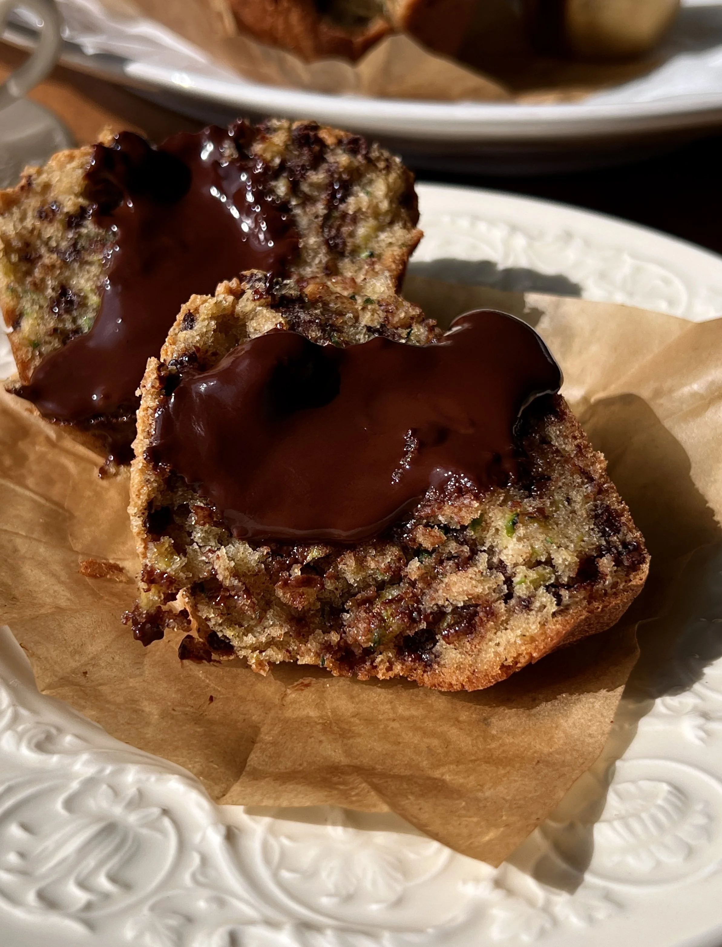 Bakery-style chocolate fudge zucchini muffin with a bite taken out showing the soft fluffy crumb, melty chocolate chips, and warm molten chocolate ganache center throughout.