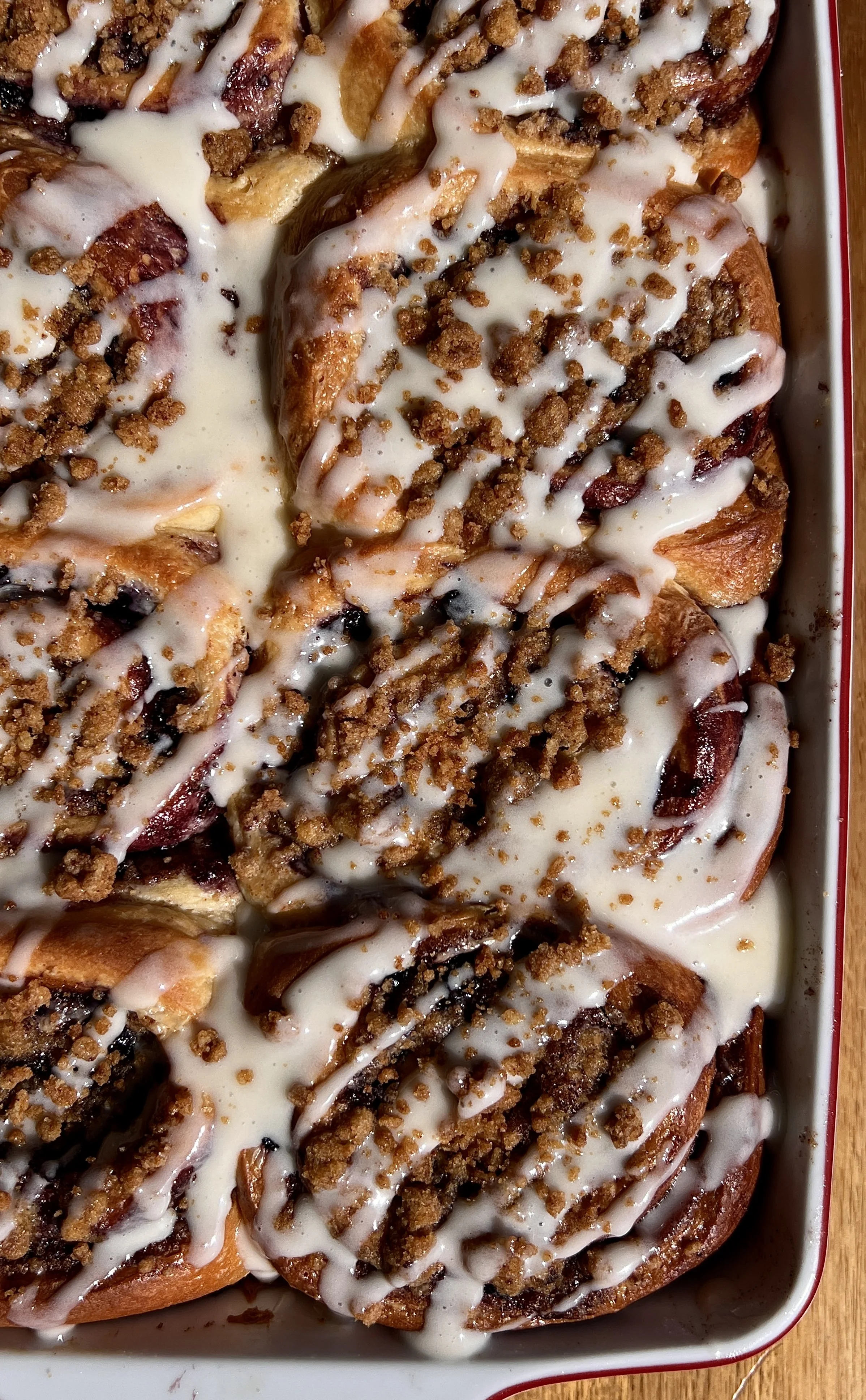 Blueberry cinnamon rolls with golden edges, crumb topping, and glossy vanilla glaze dripping over the top