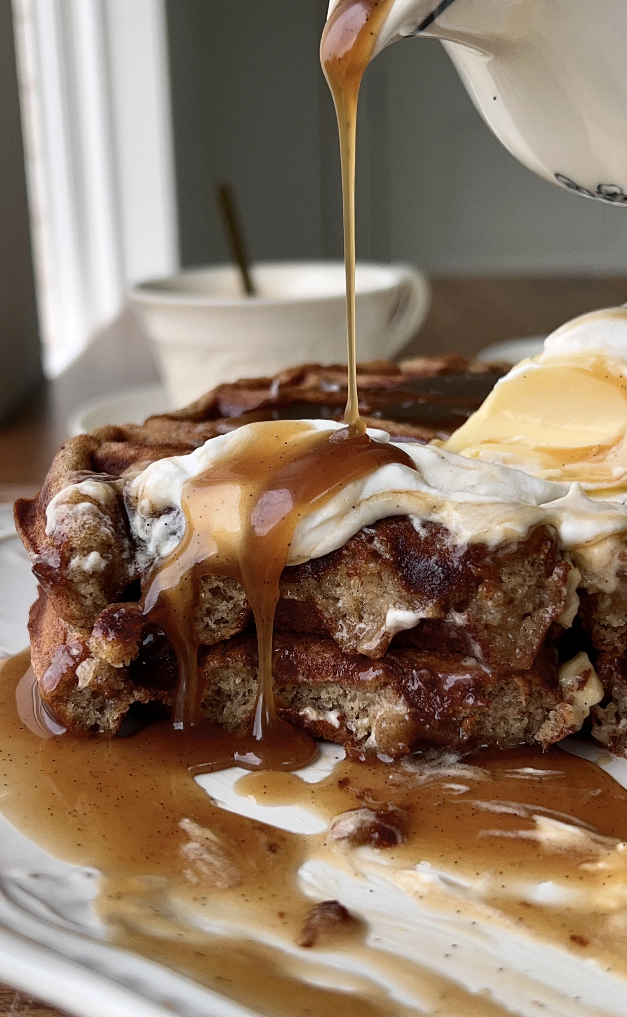 Soft and fluffy sticky toffee waffles with a perfectly golden crisp exterior served warm with butter, a dollop of whipped sour cream topping, and a drizzle of silky maple toffee sauce that melts into every nook served with a hot cup of coffee.