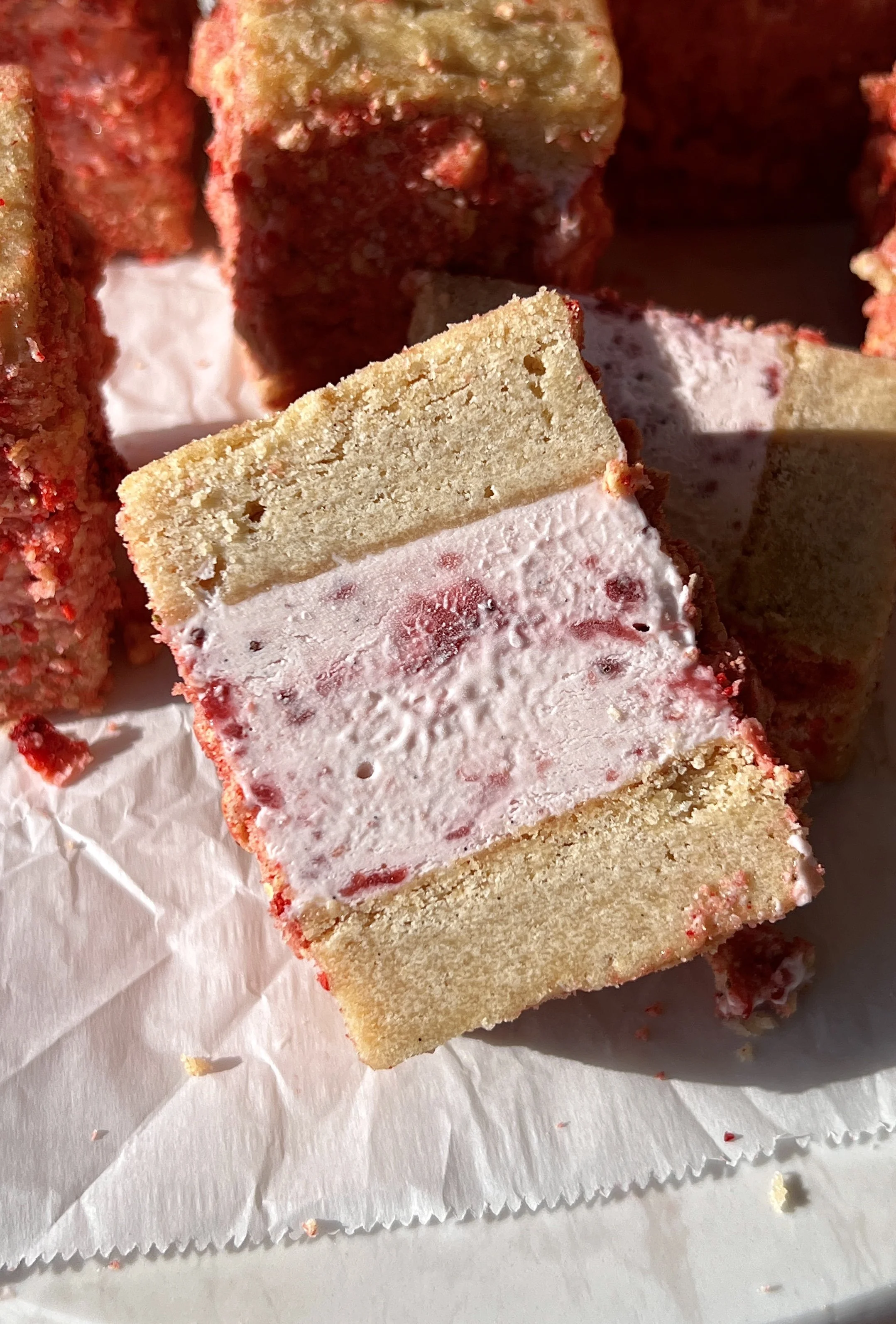 Close-up of a strawberry shortcake shortbread ice cream sandwich showing the soft buttery shortbread layers with rich and creamy homemade no-churn strawberry ice cream coated in a strawberry shortcake crunch coating throughout.
