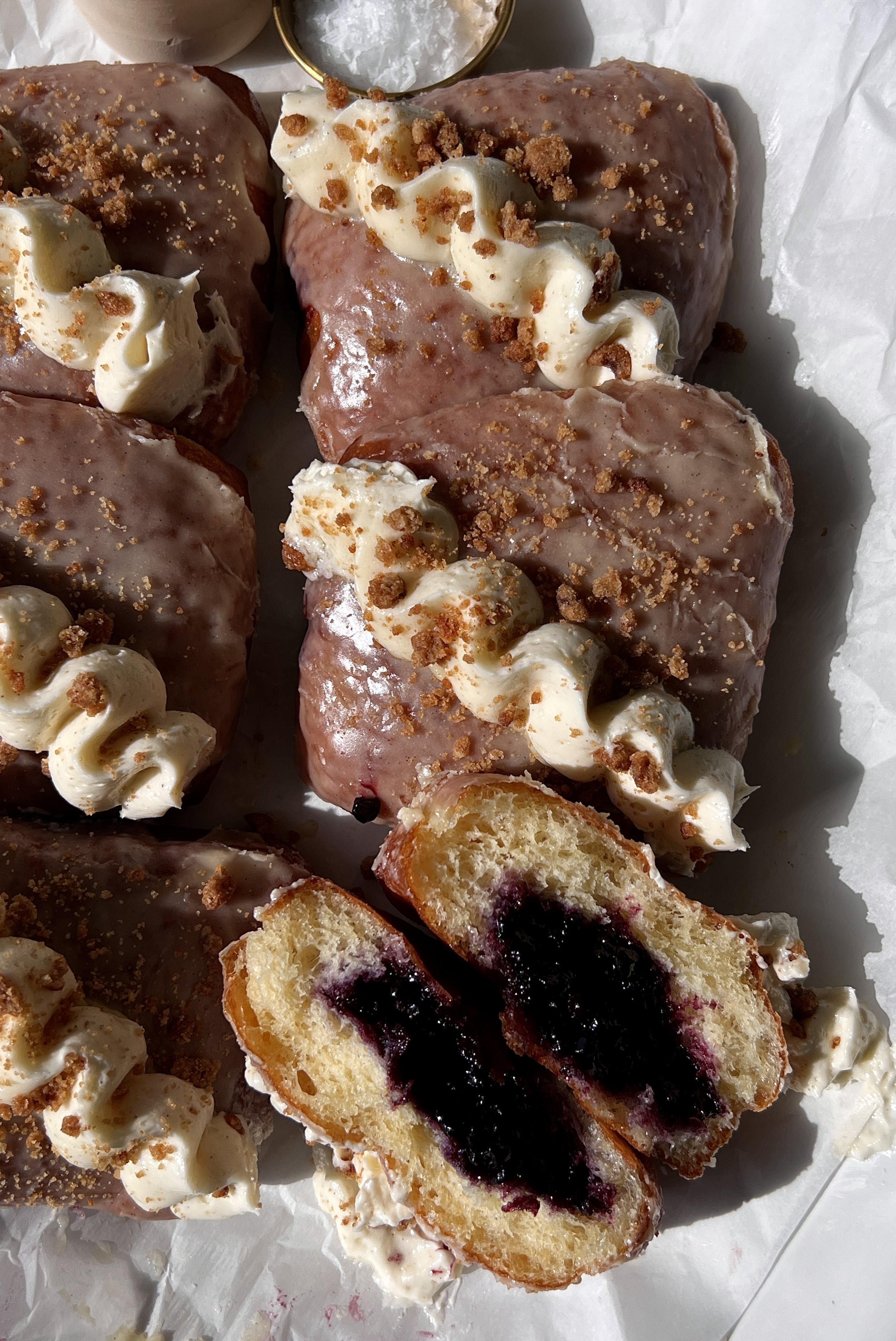 Blueberry pie donut bars coated in a silky vanilla bean glaze topped with whipped buttercream and shortbread crumbles served warm with a hot cup of coffee.