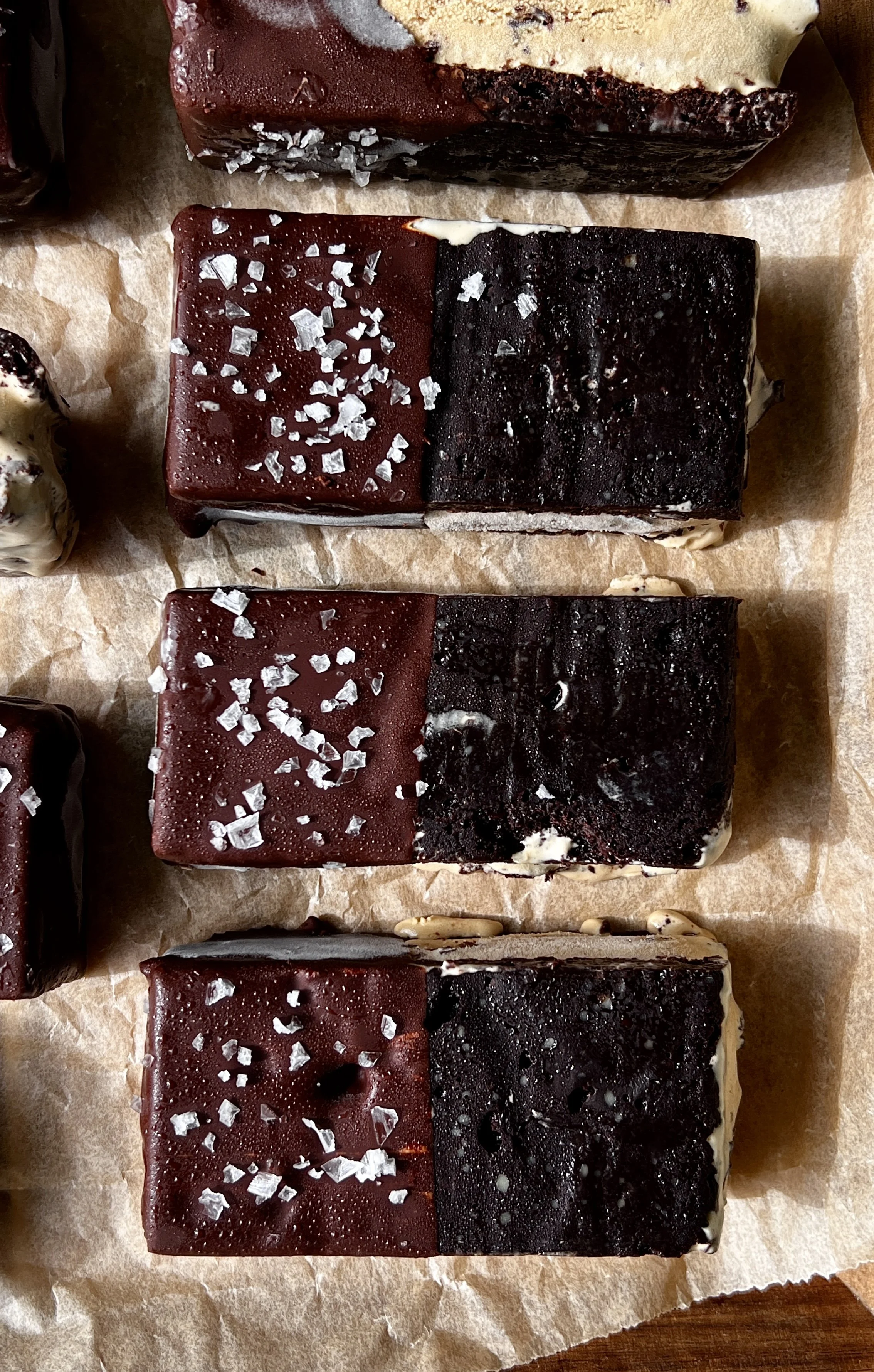 Close-up of a brownie ice cream sandwich showing the fudgy brownie layers with rich and creamy coffee chip ice cream and chocolate chunks throughout dipped in chocolate.
