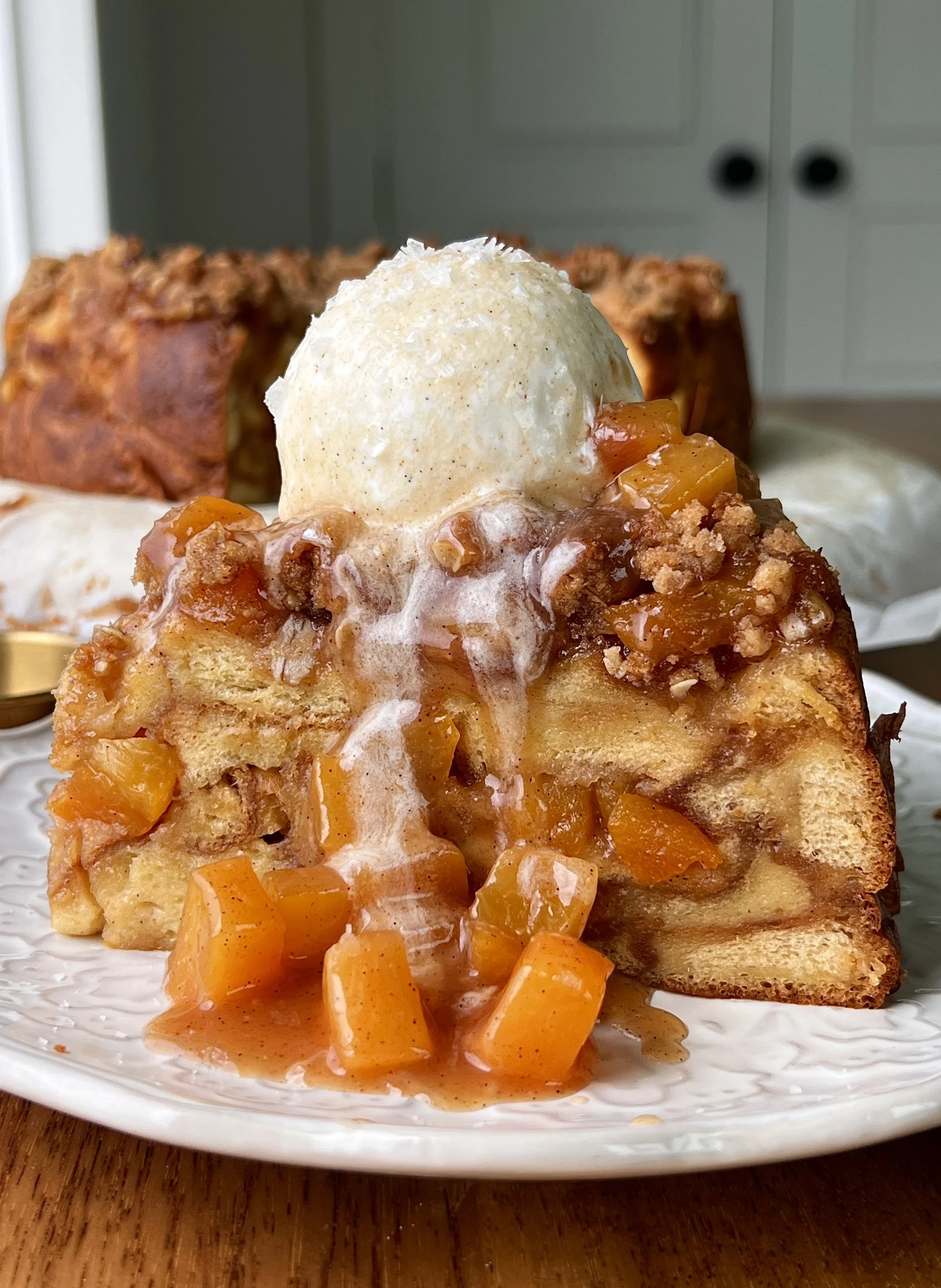 Peach cobbler buttermilk bread pudding with a golden oat streusel served warm with a scoop of vanilla ice cream and flaky sea salt.