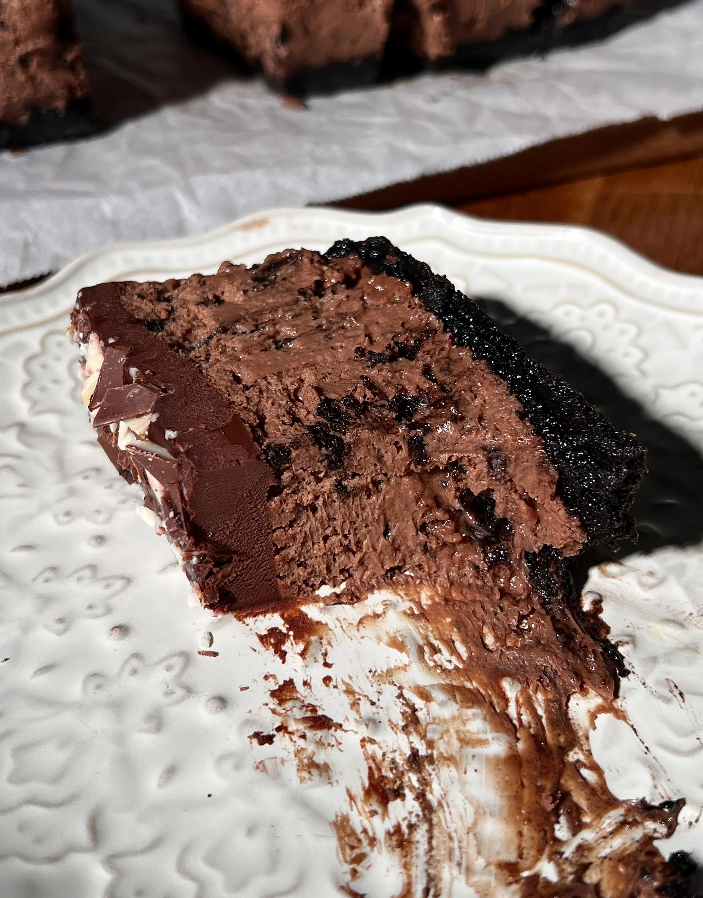 Close-up of peppermint Oreo cheesecake bars with a dark Oreo crust, creamy peppermint mocha cheesecake filling, chocolate ganache topping, and chopped peppermint bark sprinkled on top.