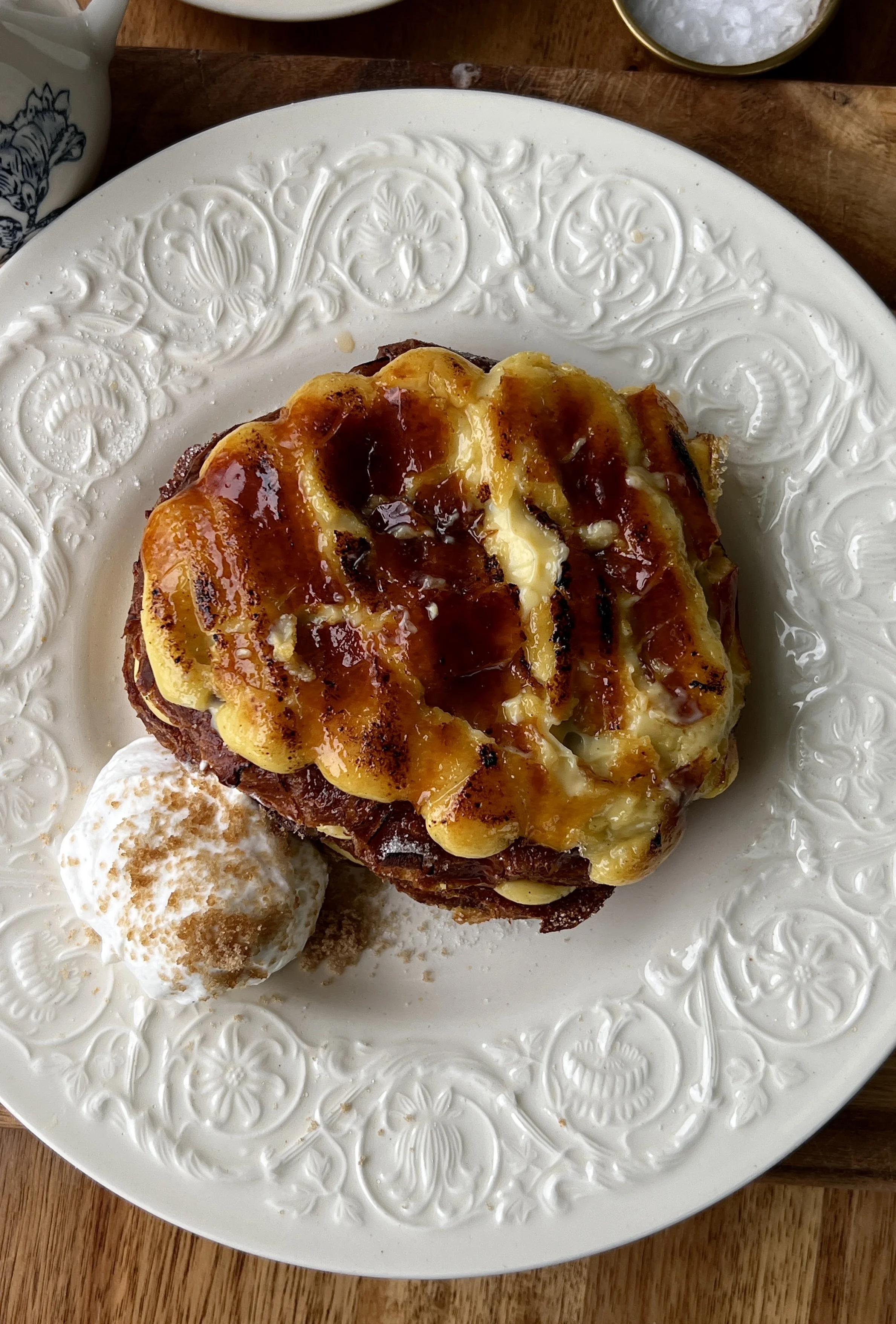 Crème brûlée croissant french toast with a crisp caramelized sugar topping served with maple syrup, whipped cream, and a hot cup of coffee.