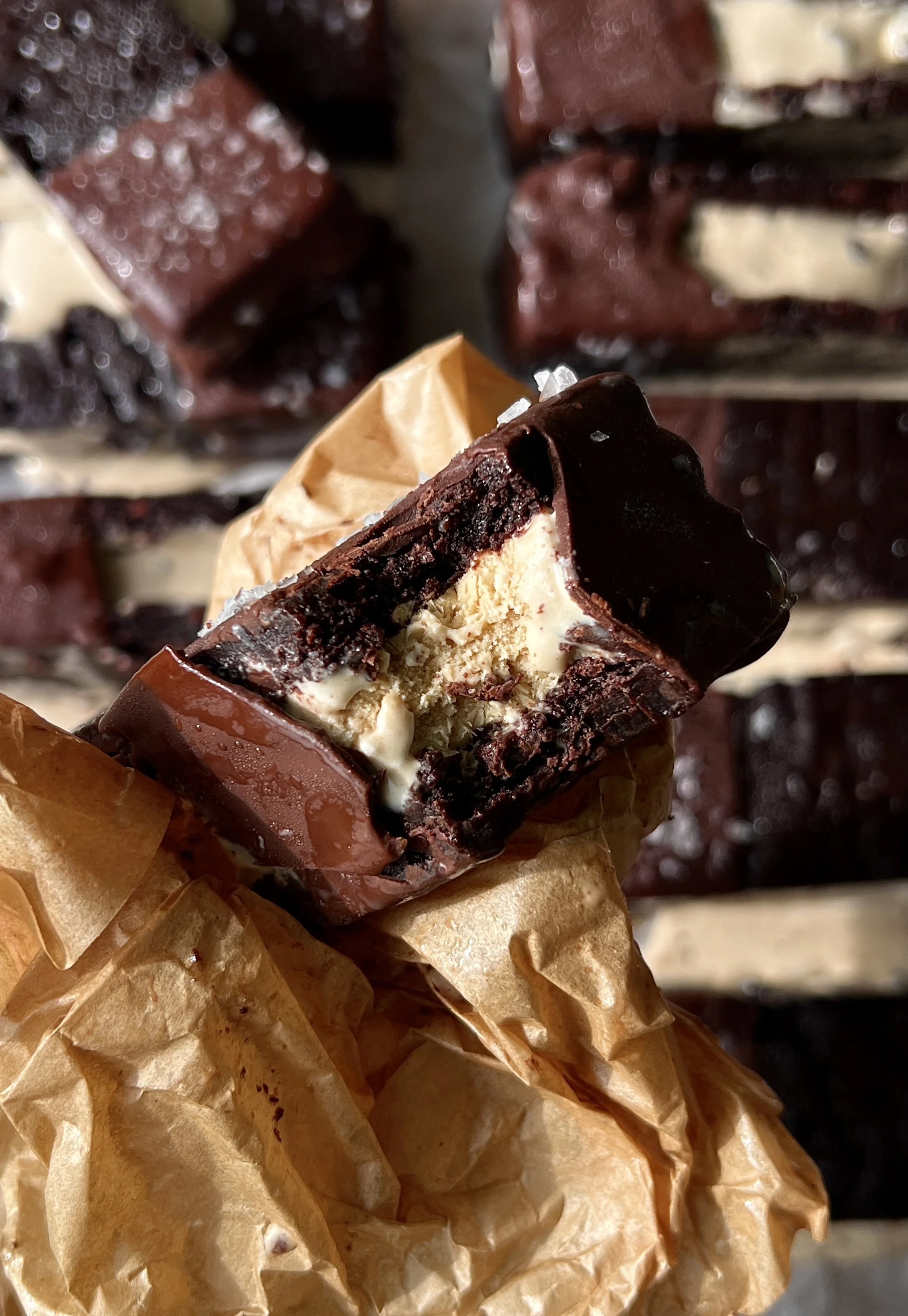 Brownie ice cream sandwich with a bite taken out showing the fudgy brownie layers with rich and creamy coffee chip ice cream loaded with chocolate chunks inside dipped in chocolate.