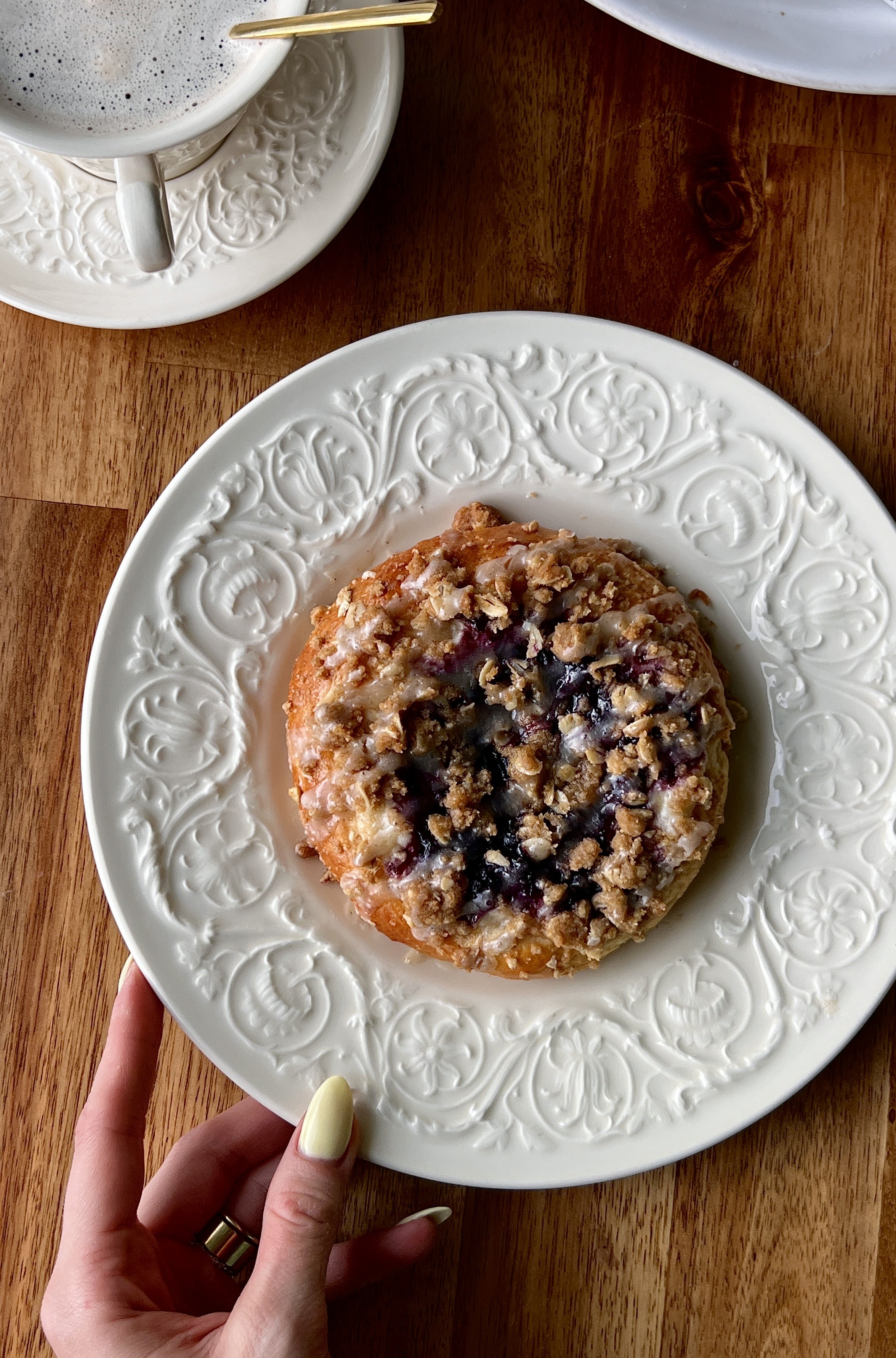 Close-up of a soft and pillowy blueberry cheesecake streusel bun with a rich and tangy cheesecake filling, homemade jammy blueberry compote, and golden oat streusel throughout.