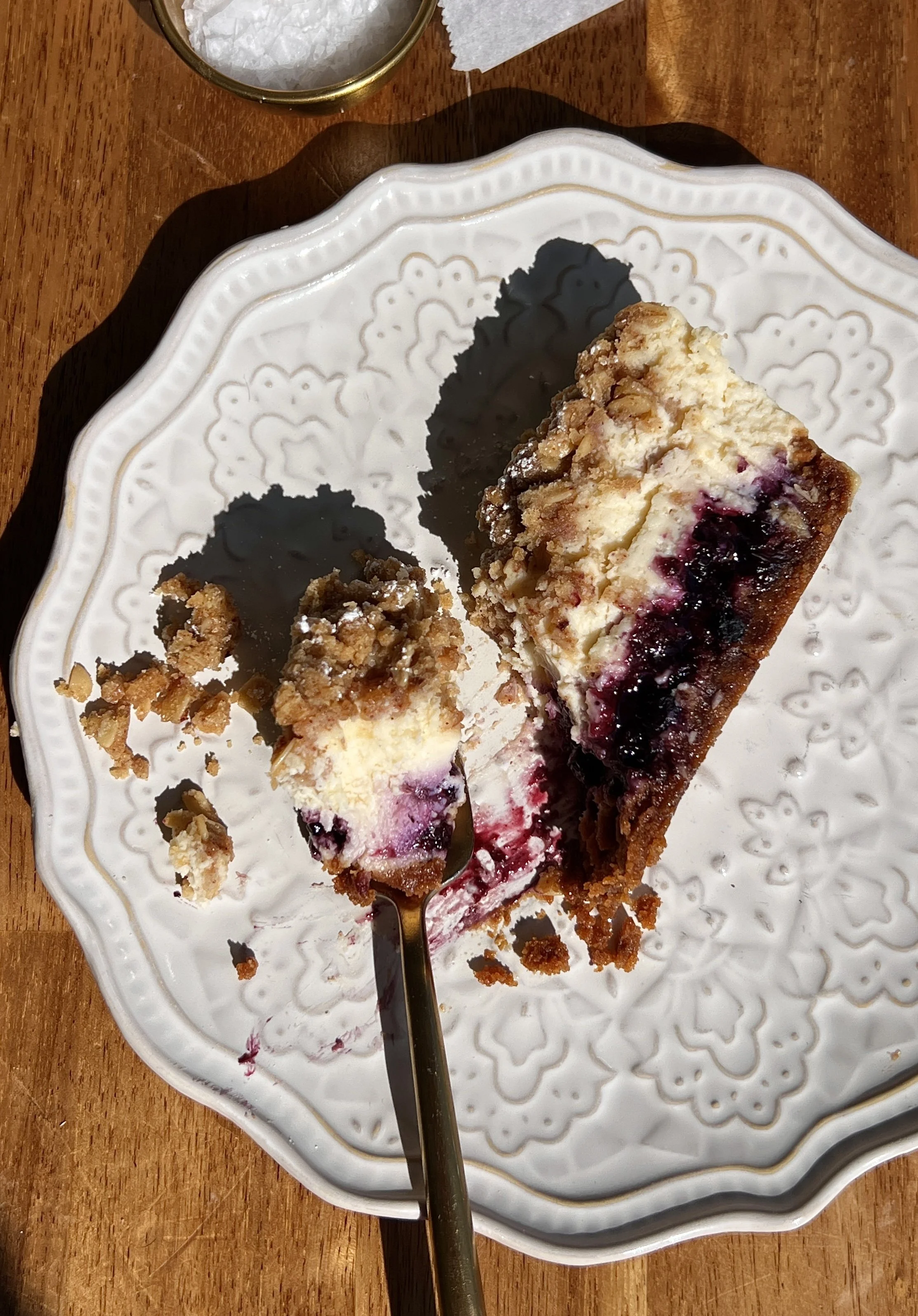 Blueberry crumble cheesecake bars with a buttery Biscoff cookie crust, tangy vanilla bean cheesecake filling, homemade blueberry compote, and golden crumble topping served on a plate.