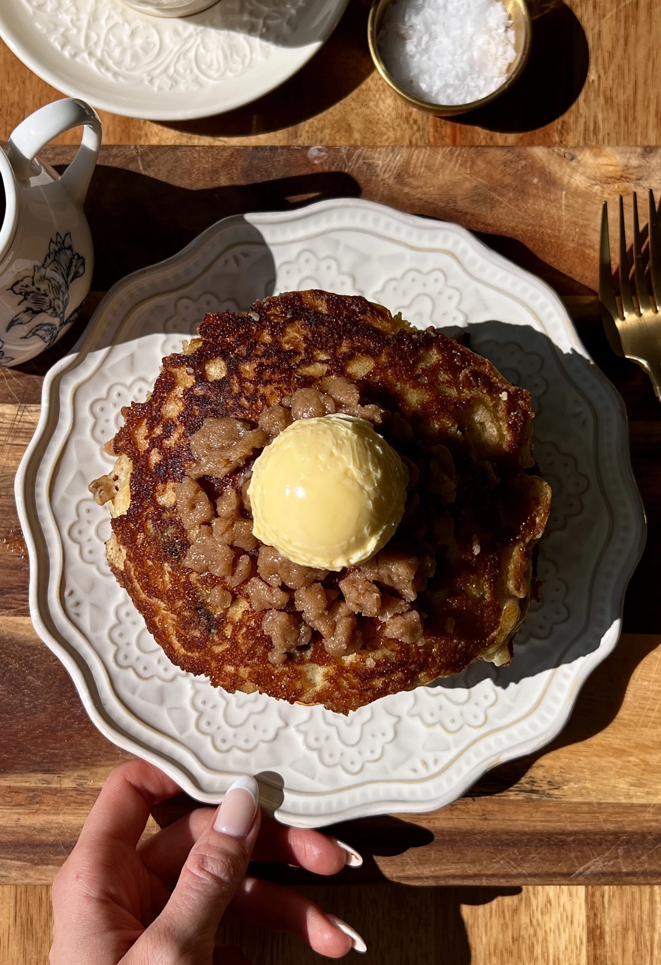 Stack of golden brown butter blueberry muffin pancakes with caramelized cinnamon streusel and juicy blueberries served warm with a pat of butter, maple syrup, and a hot cup of coffee.