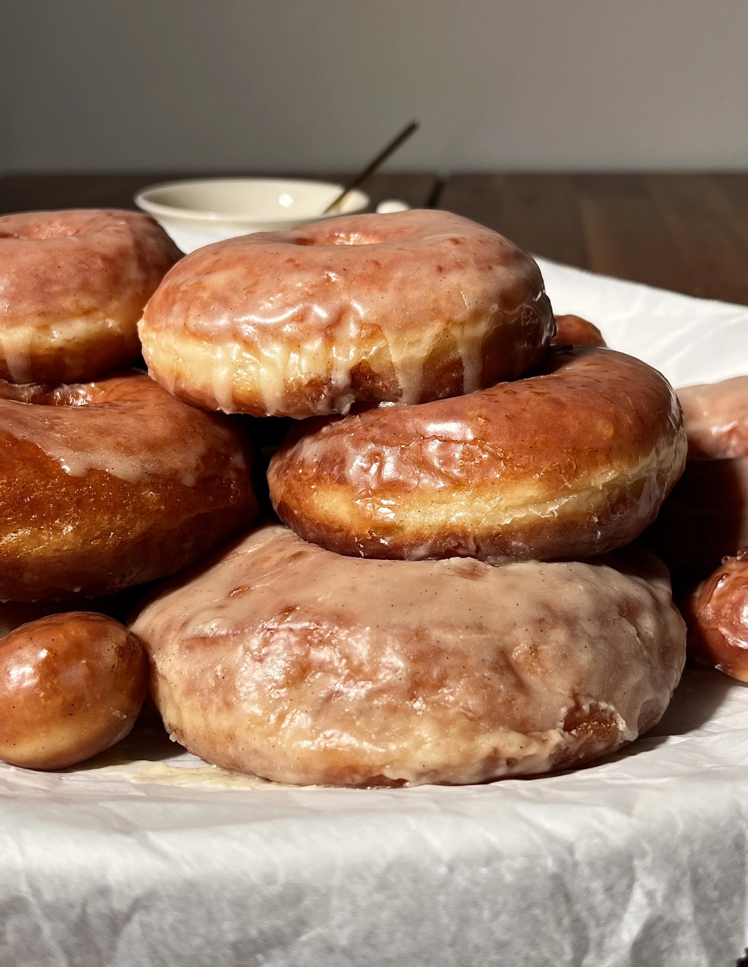 Classic vanilla bean glazed donuts served warm, showing a golden exterior and soft, pillowy interior, coated in a crackly vanilla bean glaze with coffee on the side.