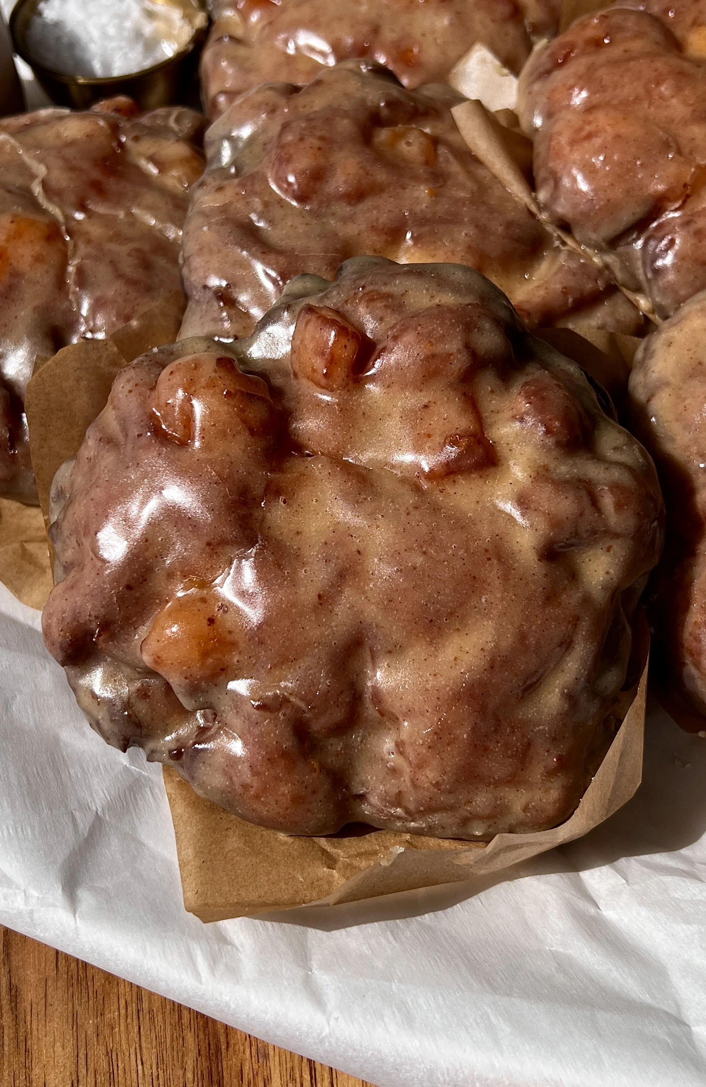 Close-up of a golden and crisp peach fritter donut with a soft and fluffy interior and warm gooey peach filling laced throughout coated in a silky brown butter maple vanilla bean glaze.