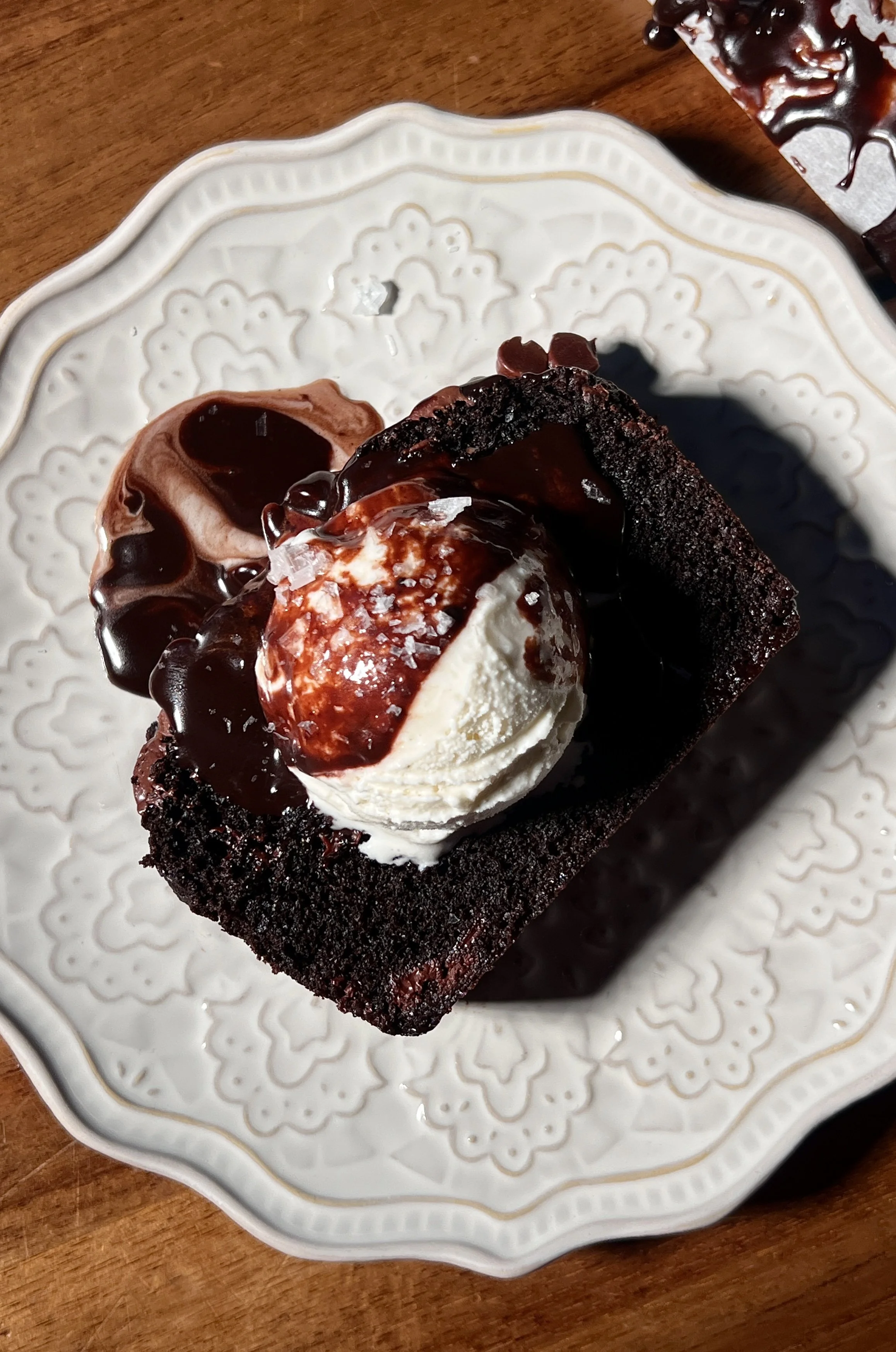 A warm and fudgy brown butter hot fudge brownie loaf with crisp edges, a gooey chocolate center, melty hot fudge sauce, vanilla ice cream, and flaky sea salt on top.