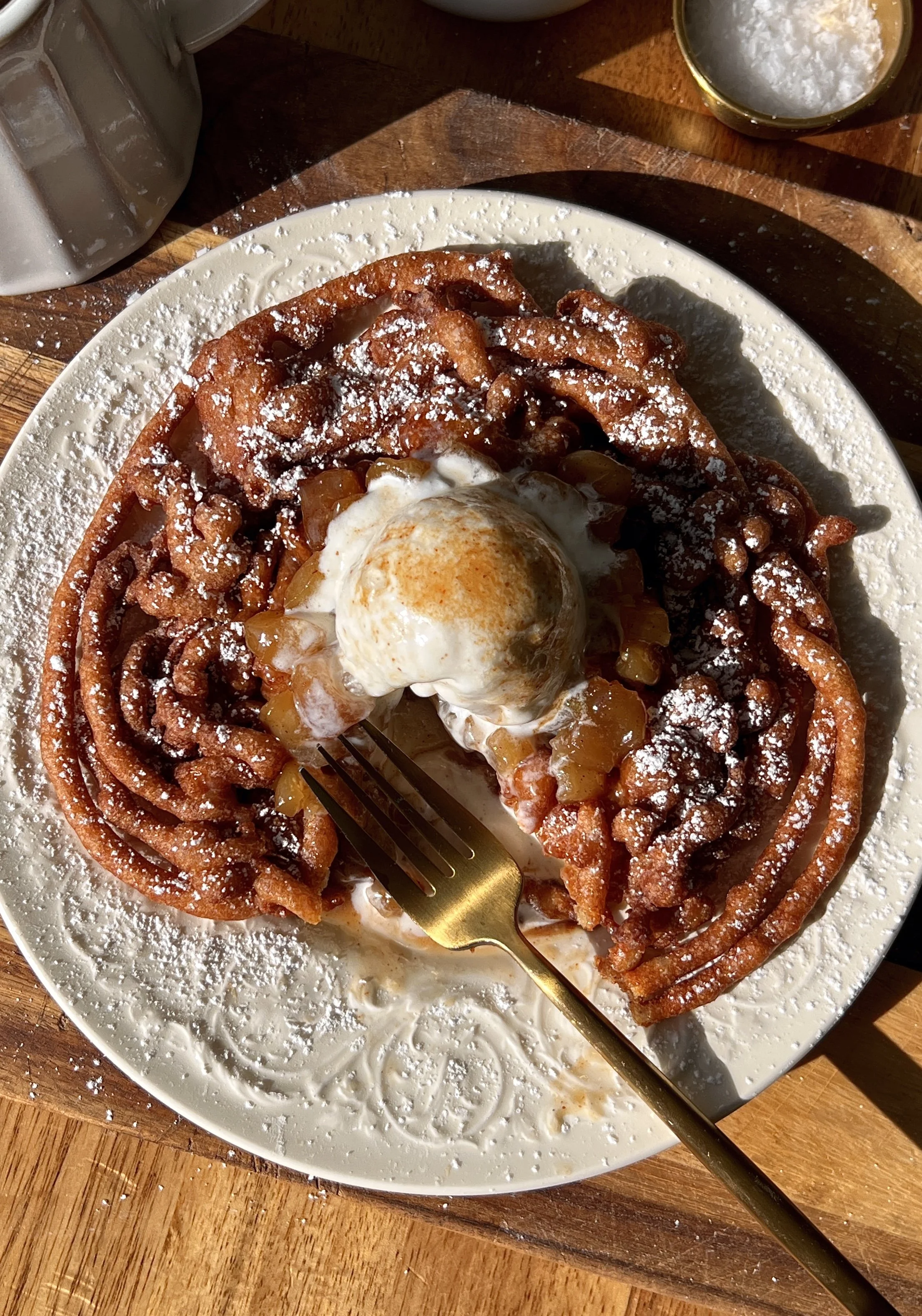 Soft and tender apple cider funnel cakes with a perfectly golden and crisp exterior served warm with a dusting of powdered sugar a gooey apple topping a scoop of vanilla ice cream and a drizzle of salted caramel.