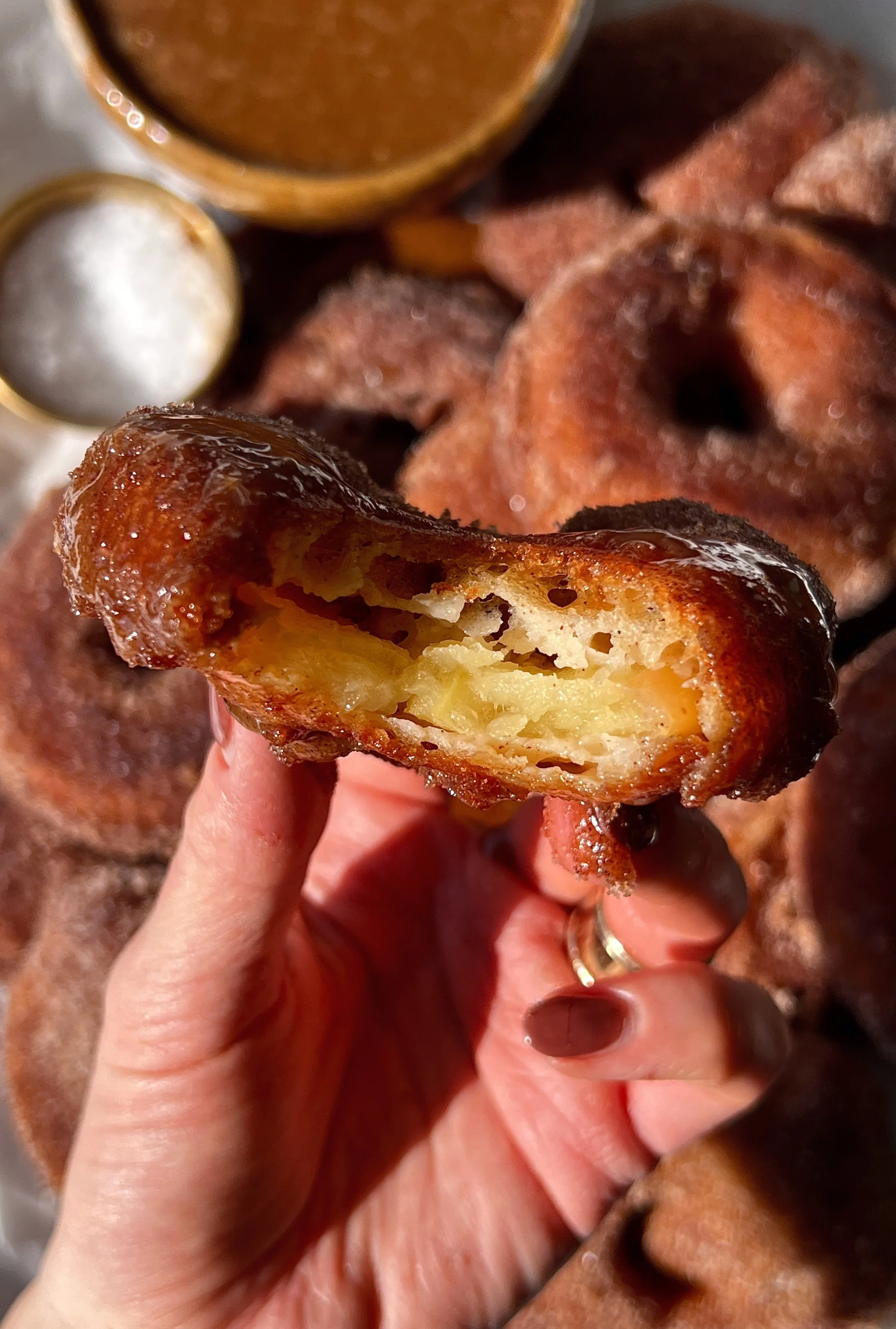 Close-up of a sourdough buttermilk fried apple ring showing the perfectly golden and crisp exterior coated in cinnamon sugar with a sweet and tart juicy apple center.