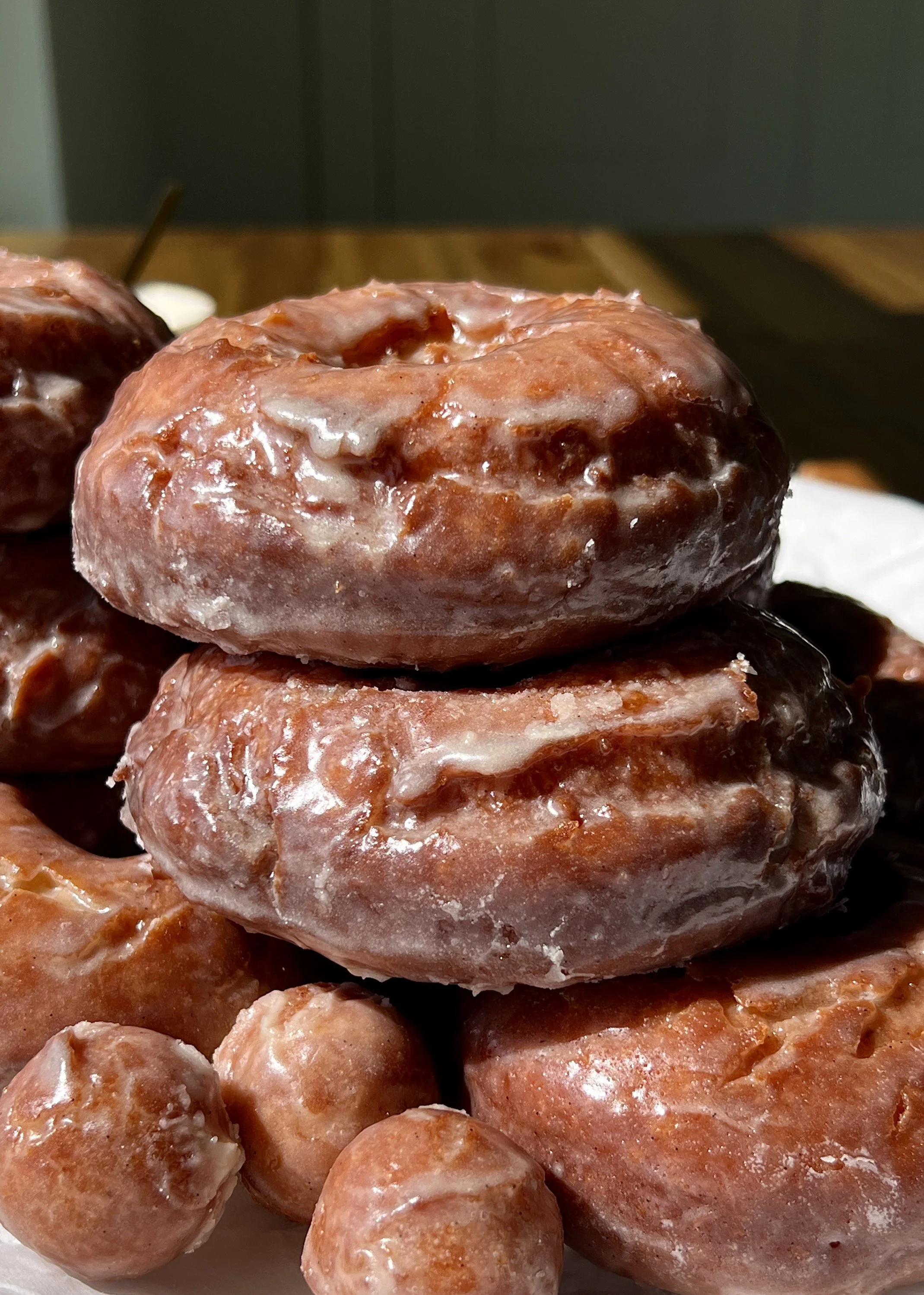 Stack of golden old-fashioned sour cream donuts coated in a silky vanilla bean glaze served warm with a hot cup of coffee.