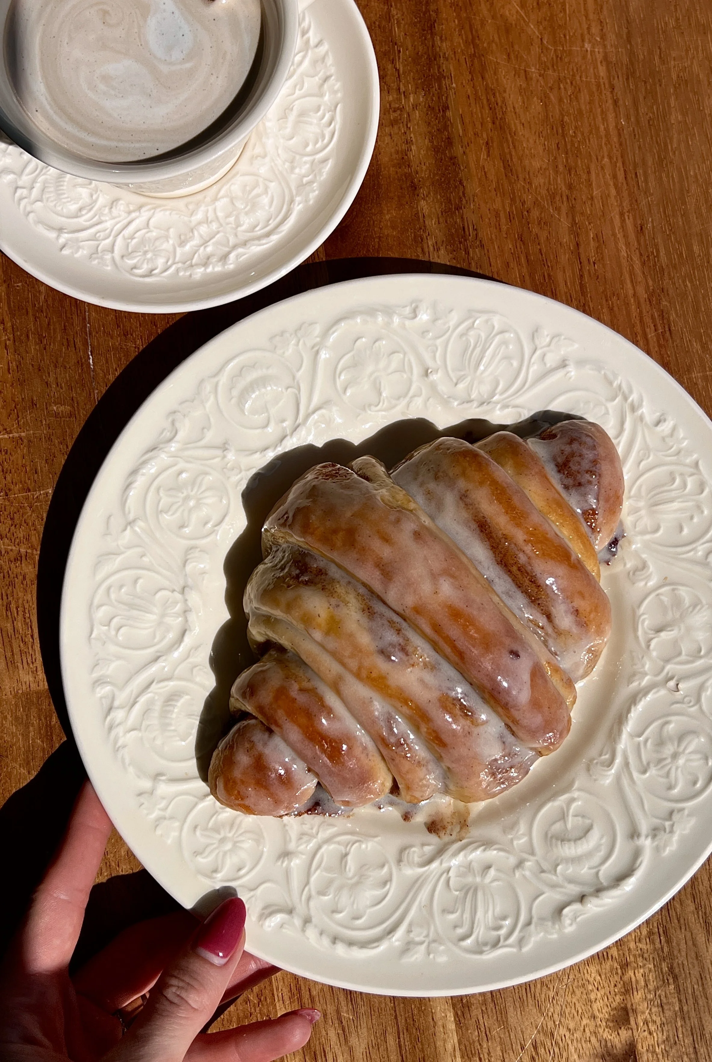 Warm cinnamon roll croissants served with cream cheese glaze and a hot cup of coffee.