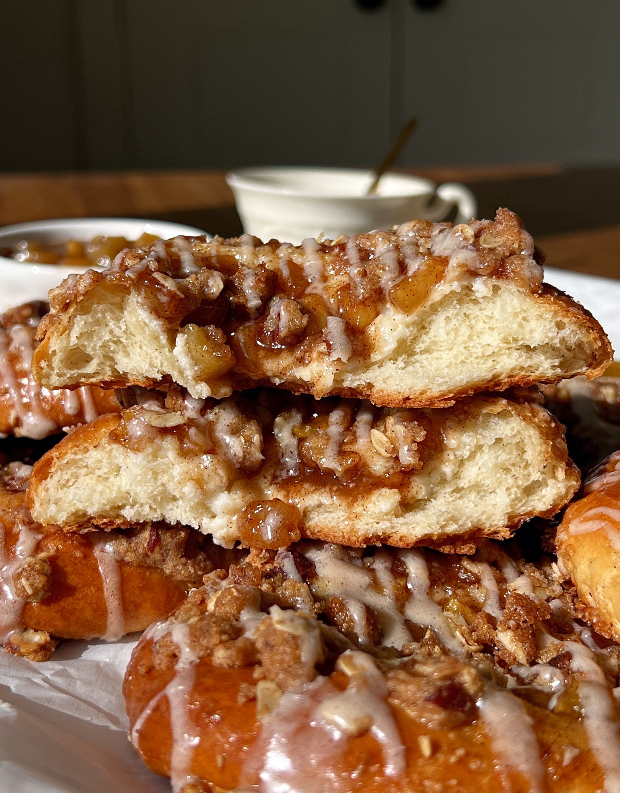 Apple streusel cheesecake buns being pulled apart showing the soft pillowy tender dough with a rich tangy cheesecake filling and warm homemade apple pie filling inside with a pecan oat streusel and maple vanilla bean glaze melting over the top.