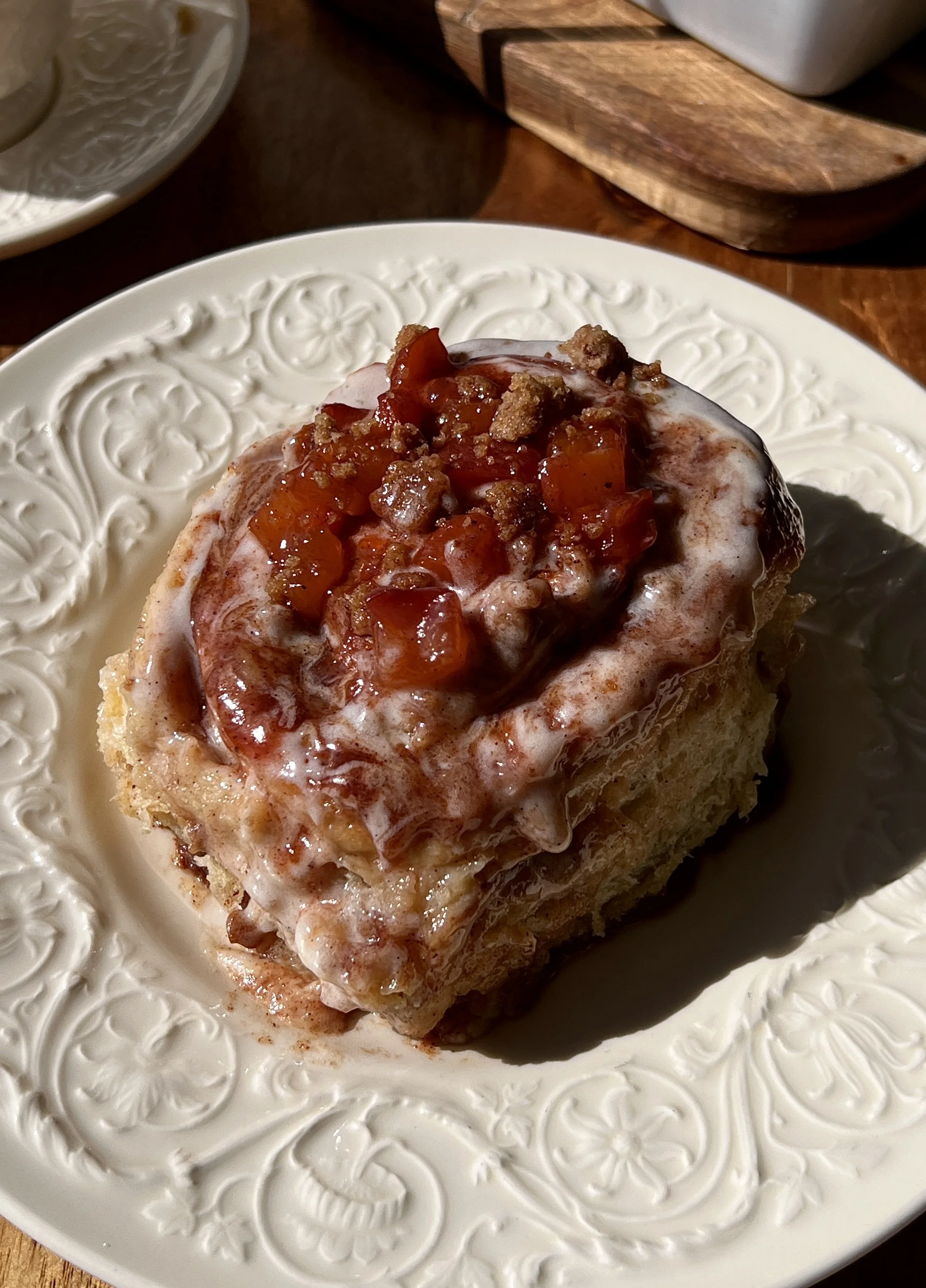 Peach cobbler cinnamon rolls with smooth cream cheese frosting served warm with a hot cup of coffee.