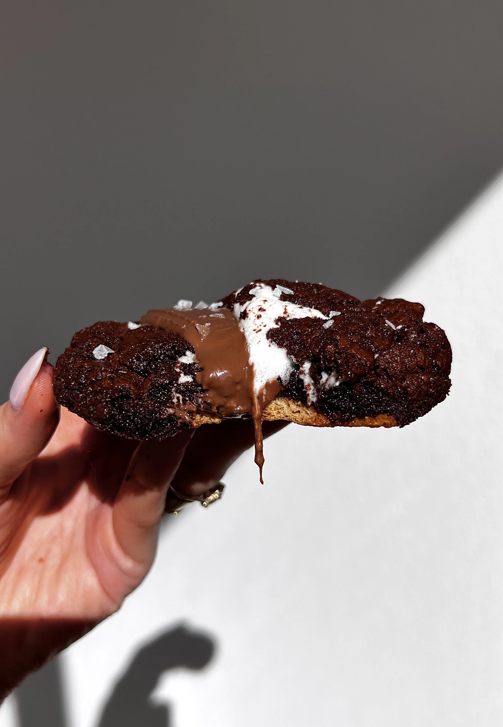 Close-up of a warm s’mores brownie cookie showing melty chocolate and gooey marshmallow filling.
