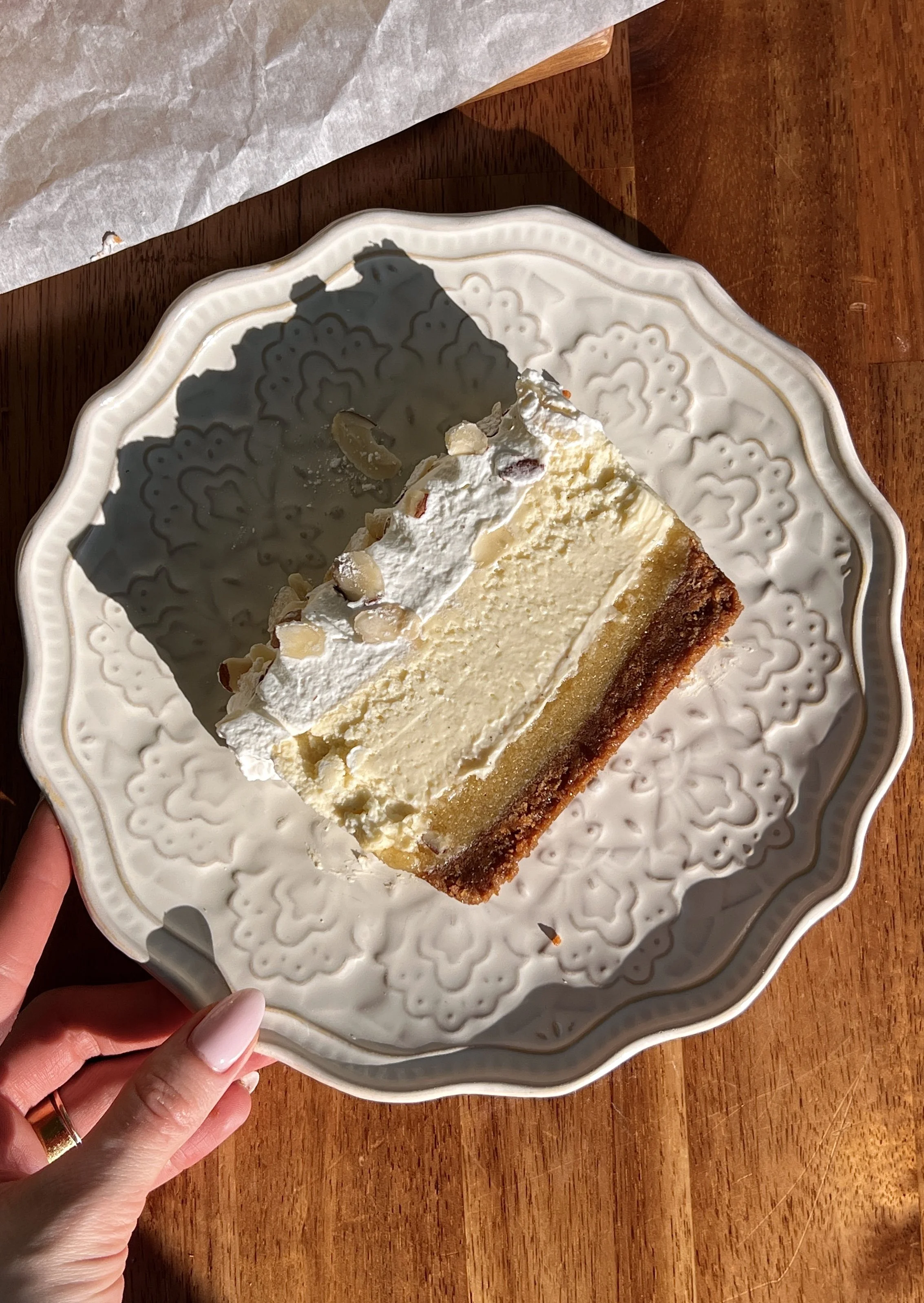 Almond frangipane cheesecake bars topped with whipped cream, sliced almonds, and powdered sugar.