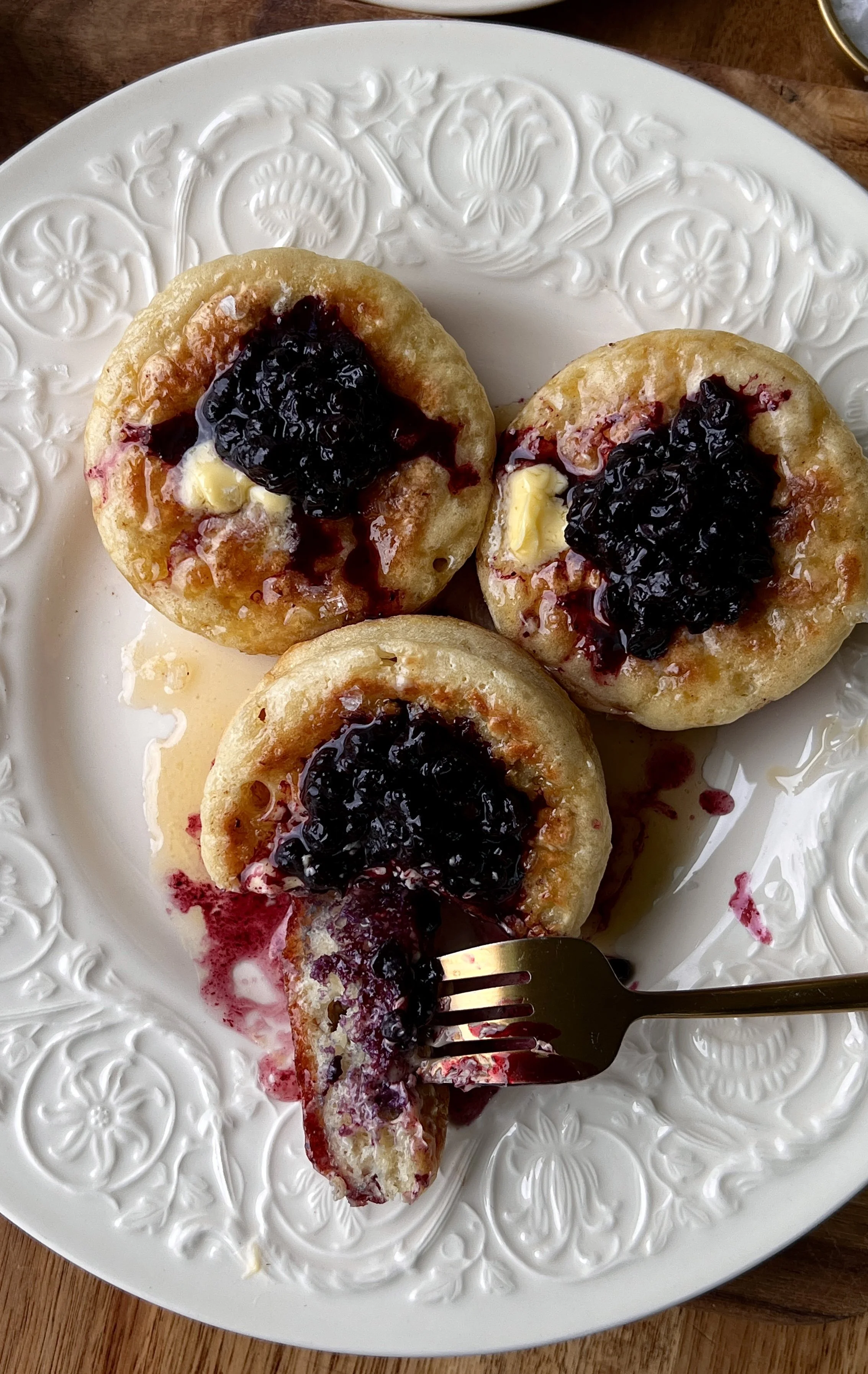 Homemade crumpets served warm with butter, blueberry compote, a drizzle of honey, and a hot cup of coffee.