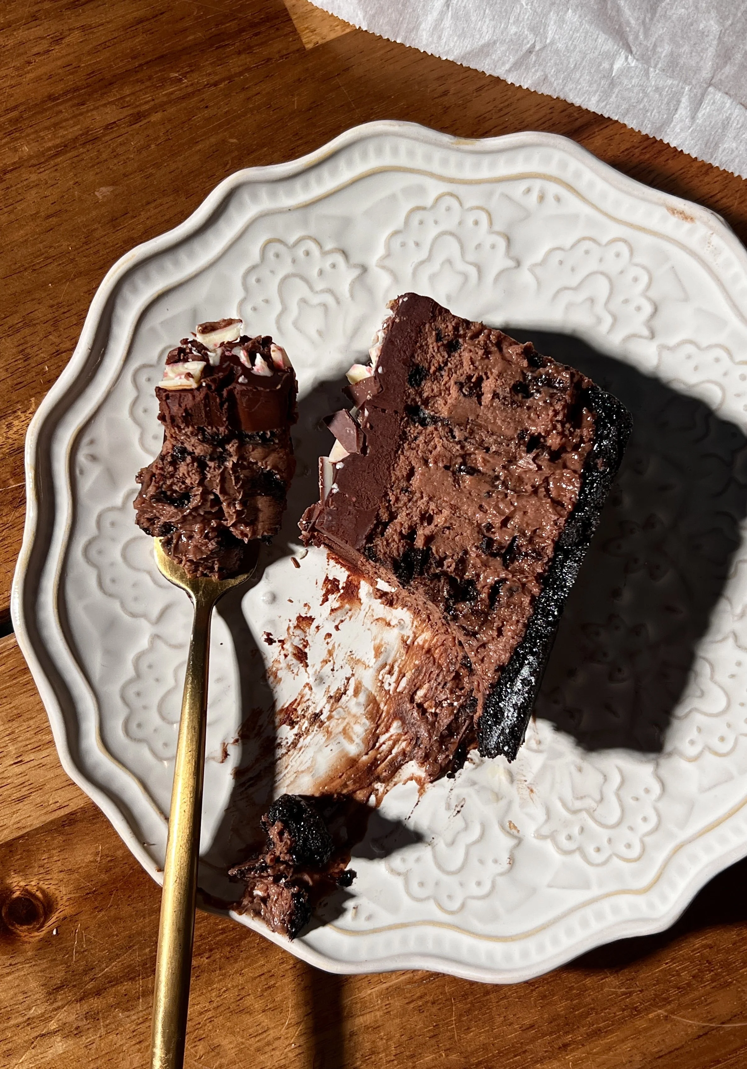 Close-up of peppermint Oreo cheesecake bars with a dark Oreo crust, creamy peppermint mocha cheesecake filling, chocolate ganache topping, and chopped peppermint bark sprinkled on top.