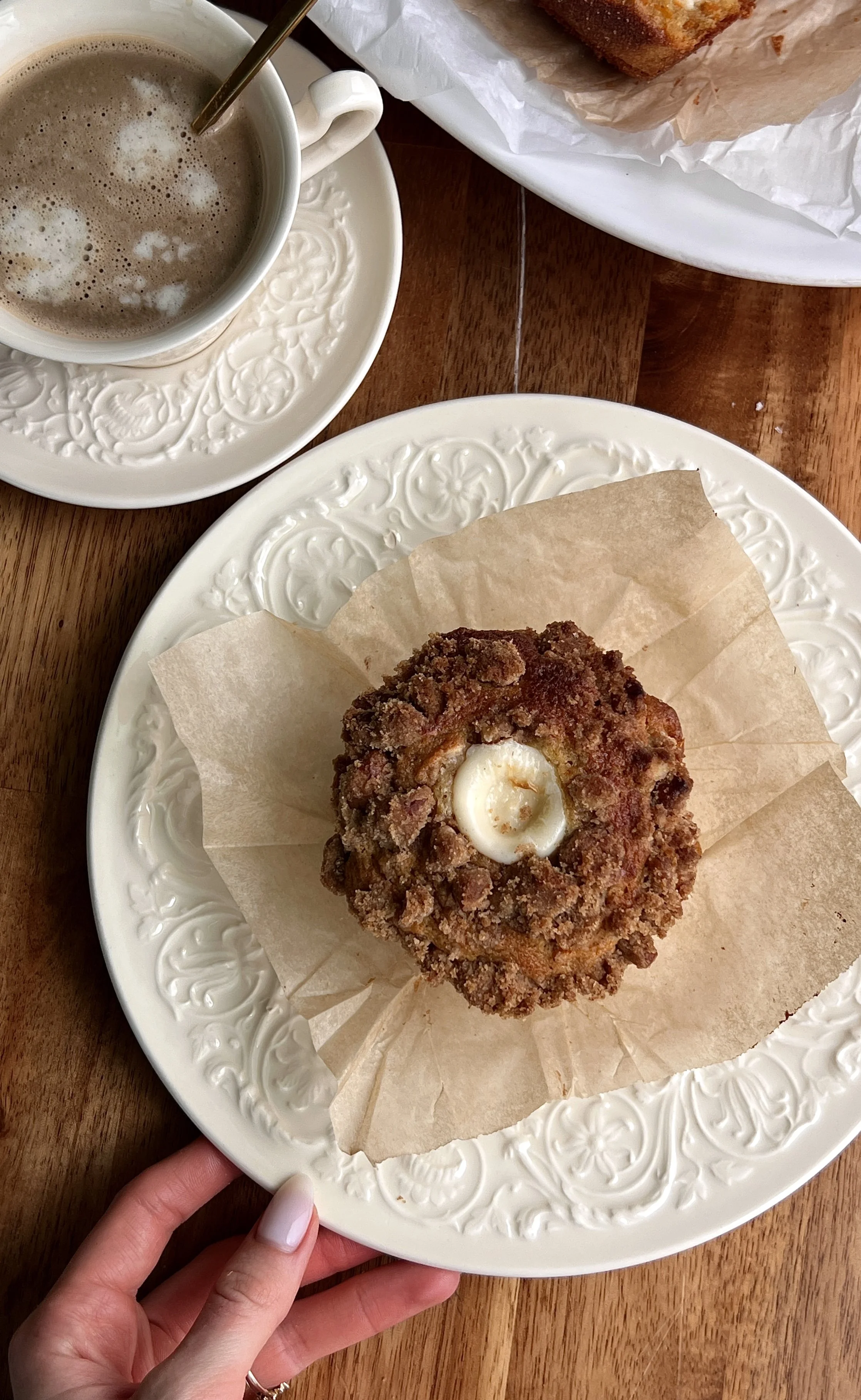 Warm carrot cake cream cheese muffins with pecan streusel served with a hot cup of coffee.