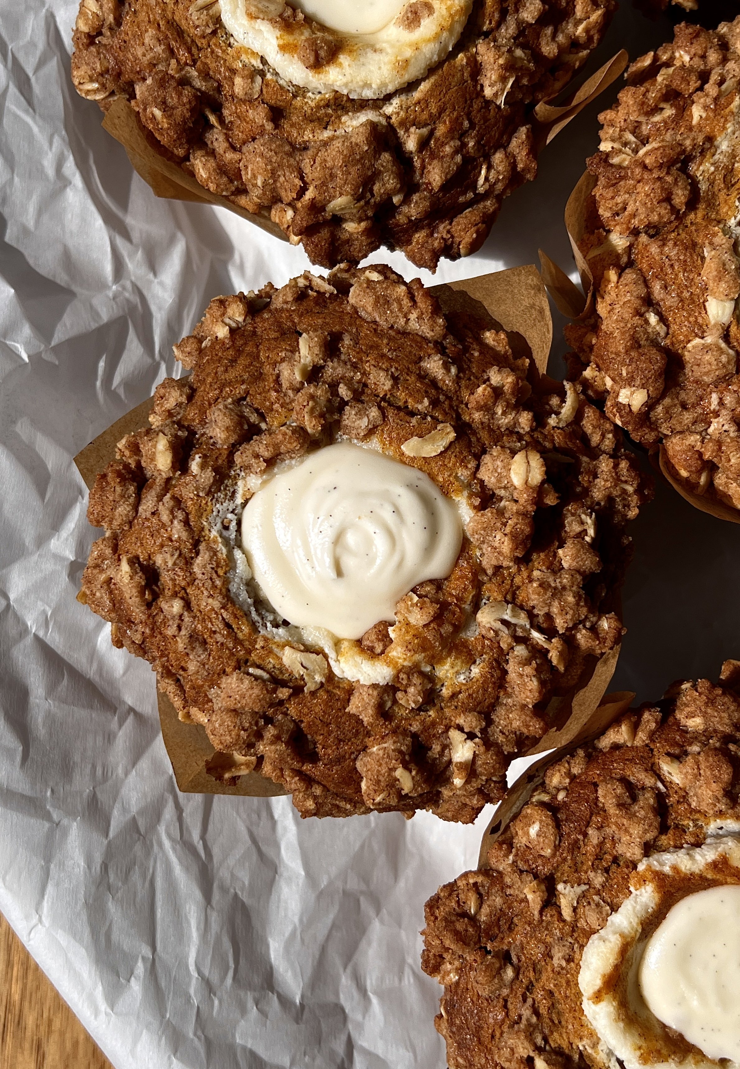 Close-up of a bakery-style pumpkin cream cheese muffin with brown butter showing the soft and fluffy delicate crumb packed with warm spiced pumpkin flavor and smooth tangy cream cheese filling with a buttery oat streusel on top.
