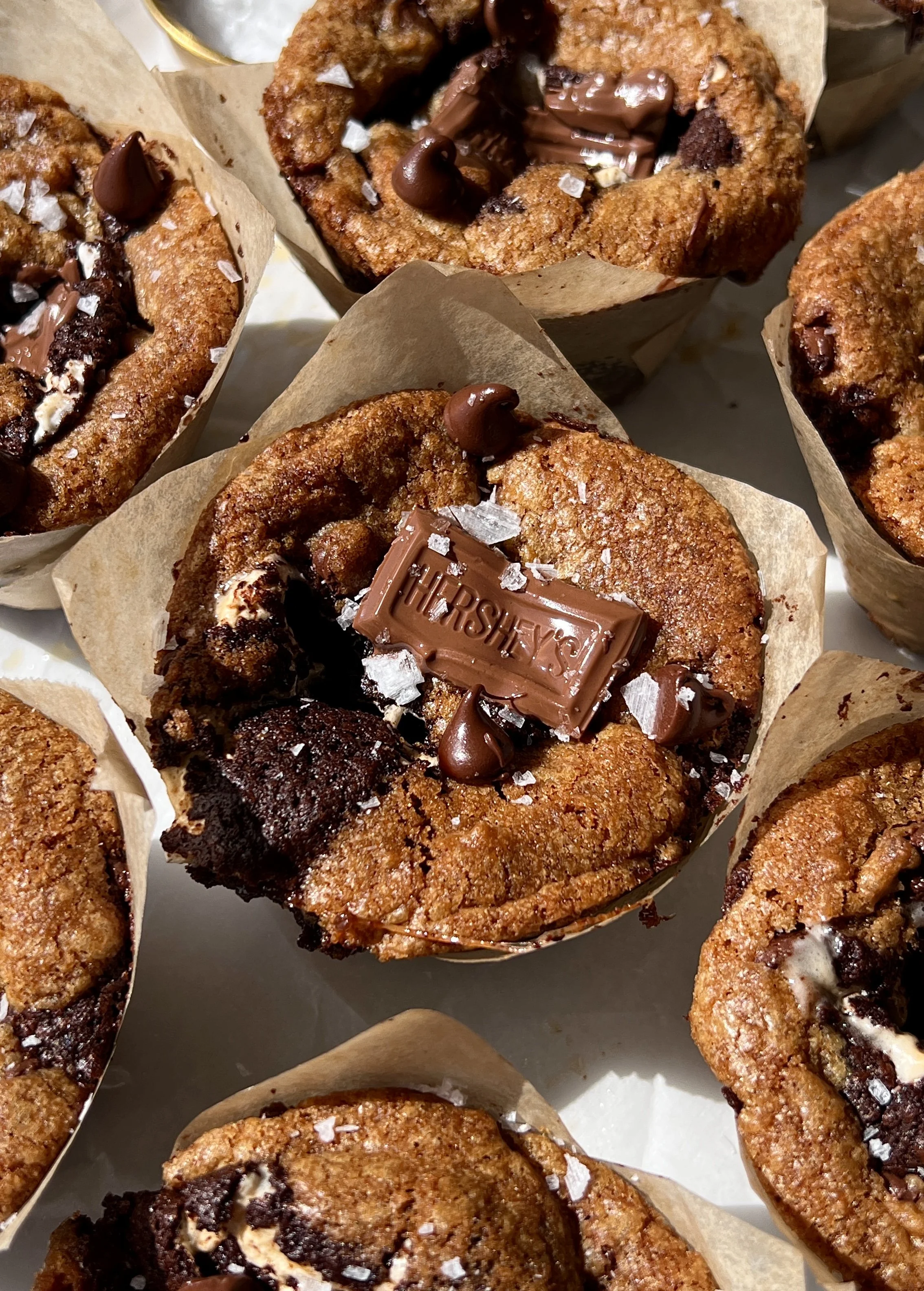 Close-up of a fudgy brown butter s'mores brookie cup with a golden crisp exterior showing the layers of brown butter cookie dough, brownie, graham cracker, marshmallow, and melty milk chocolate throughout.