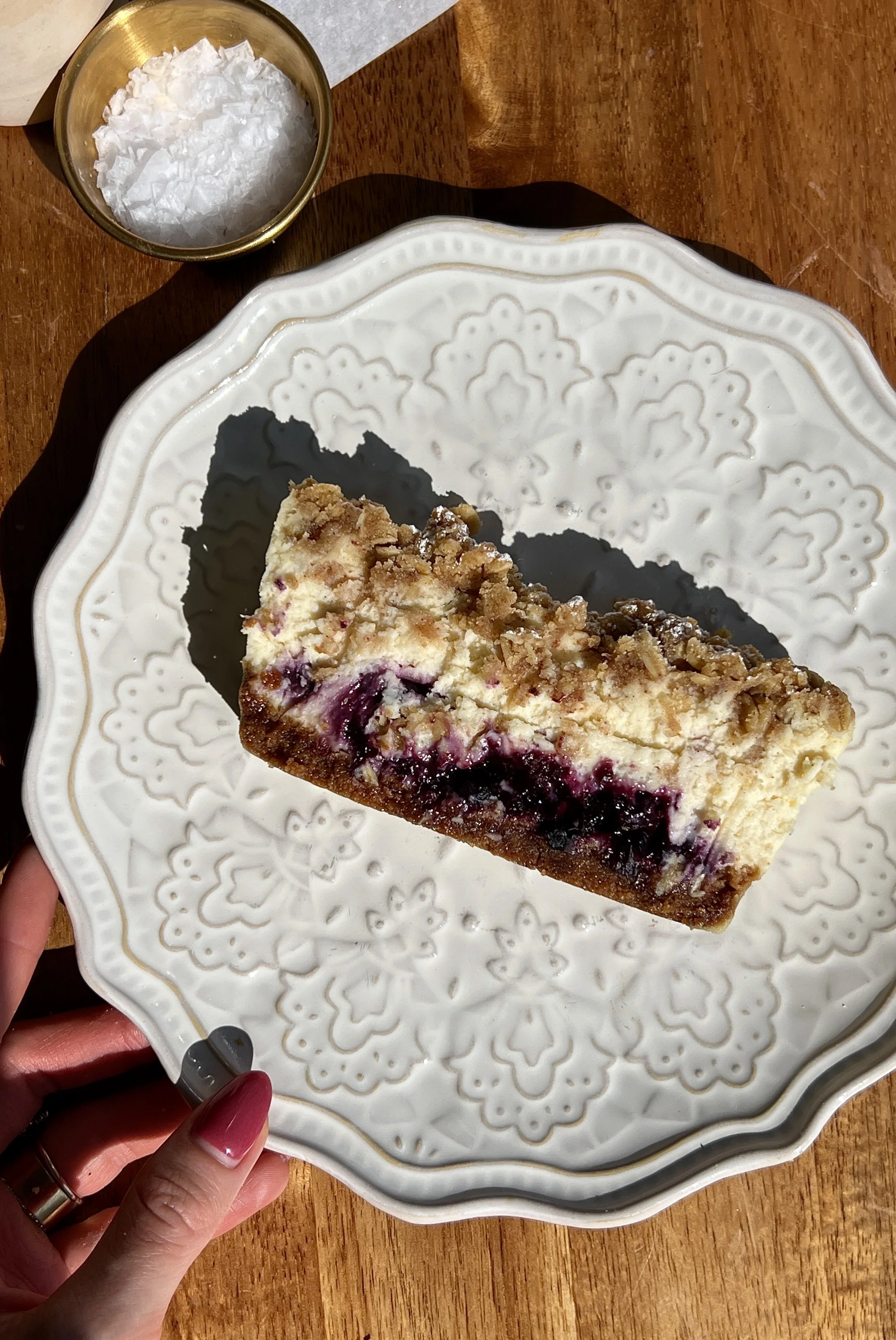 Slice of a blueberry crumble cheesecake bar showing the Biscoff cookie crust, creamy vanilla bean cheesecake filling, and blueberry compote layers.